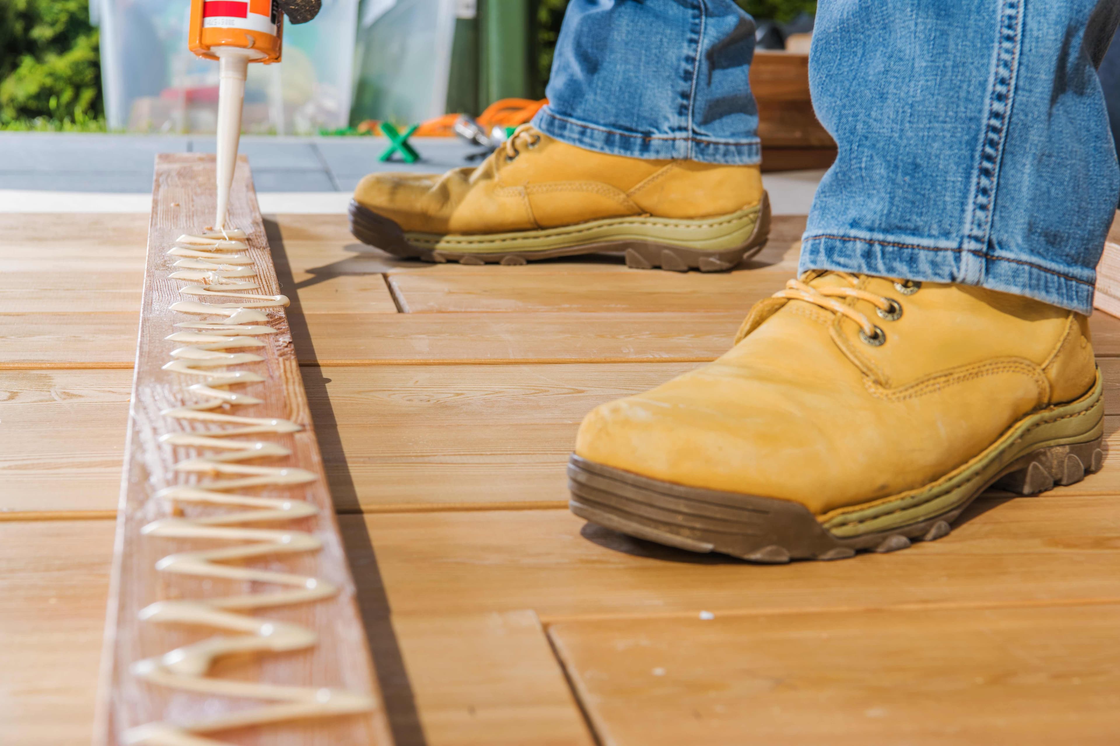 Close-up of caulk being applied along the edge of an exterior wood deck board