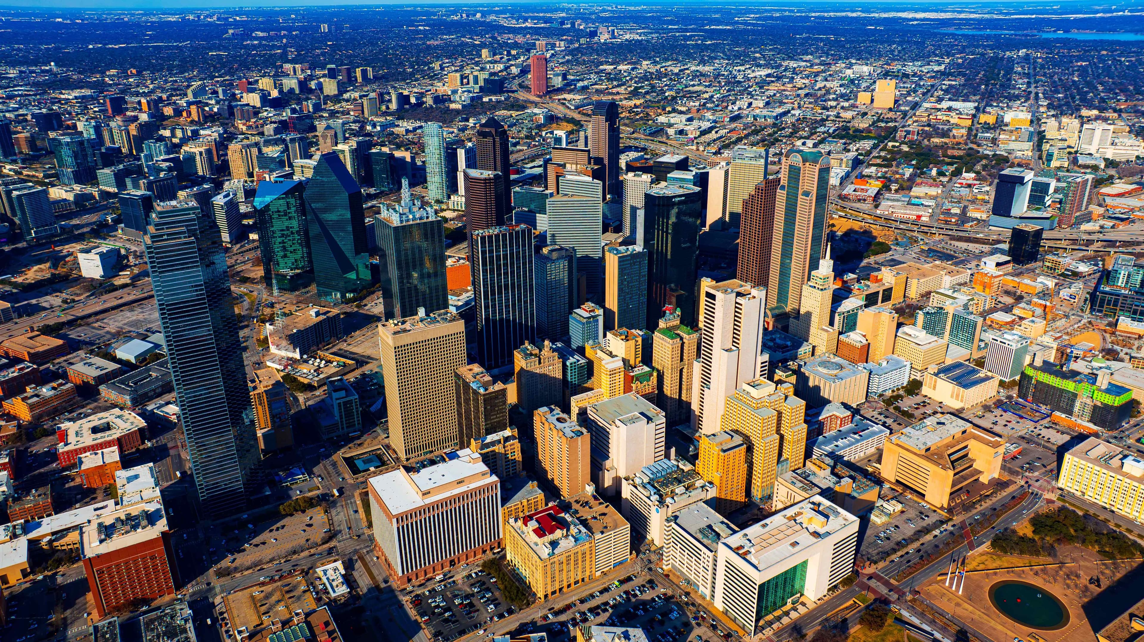 Aerial view of downtown Dallas skyscrapers and surrounding neighborhoods under a clear blue sky