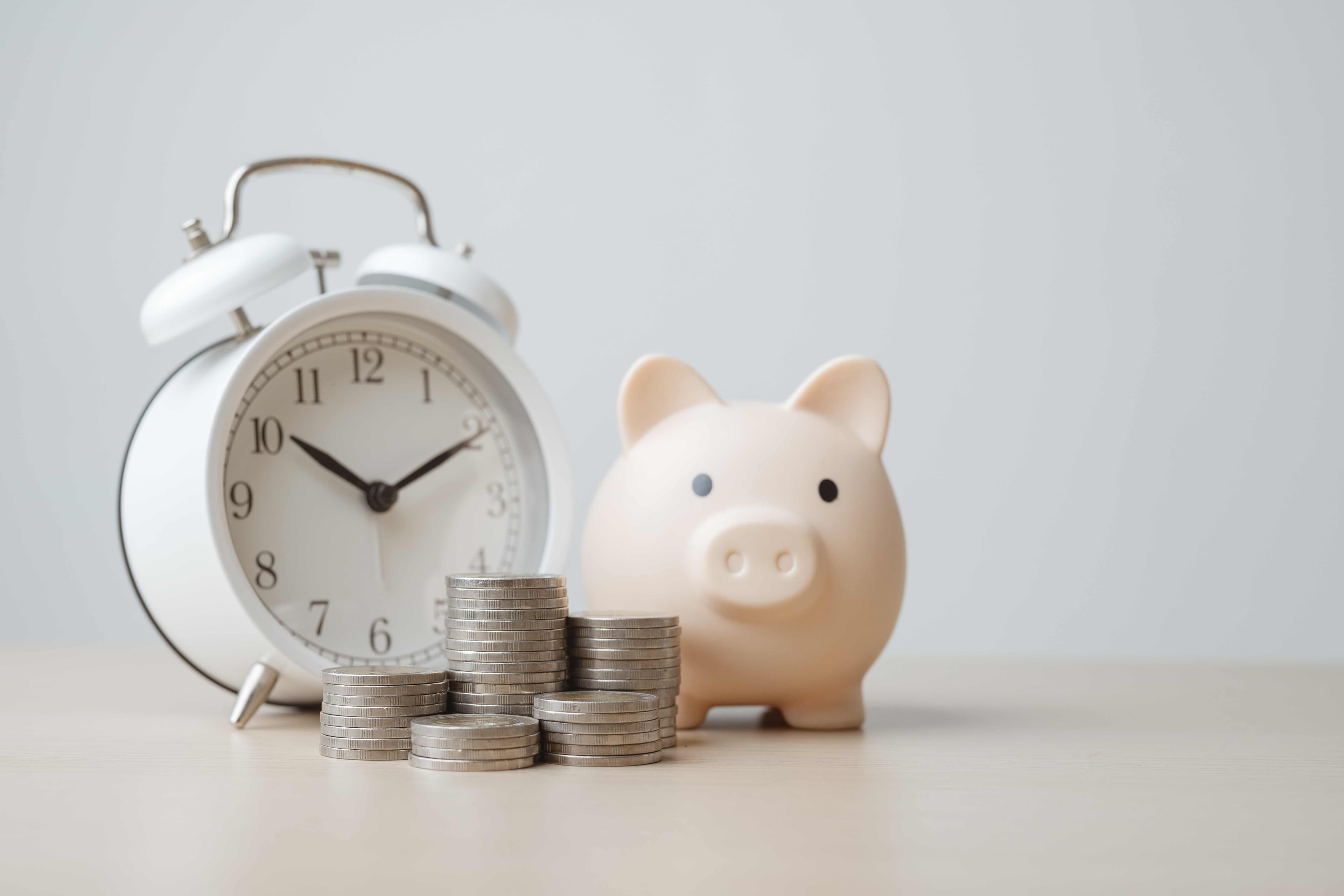 An alarm clock, a piggy bank, and stacks of coins representing a household budget and monthly bills
