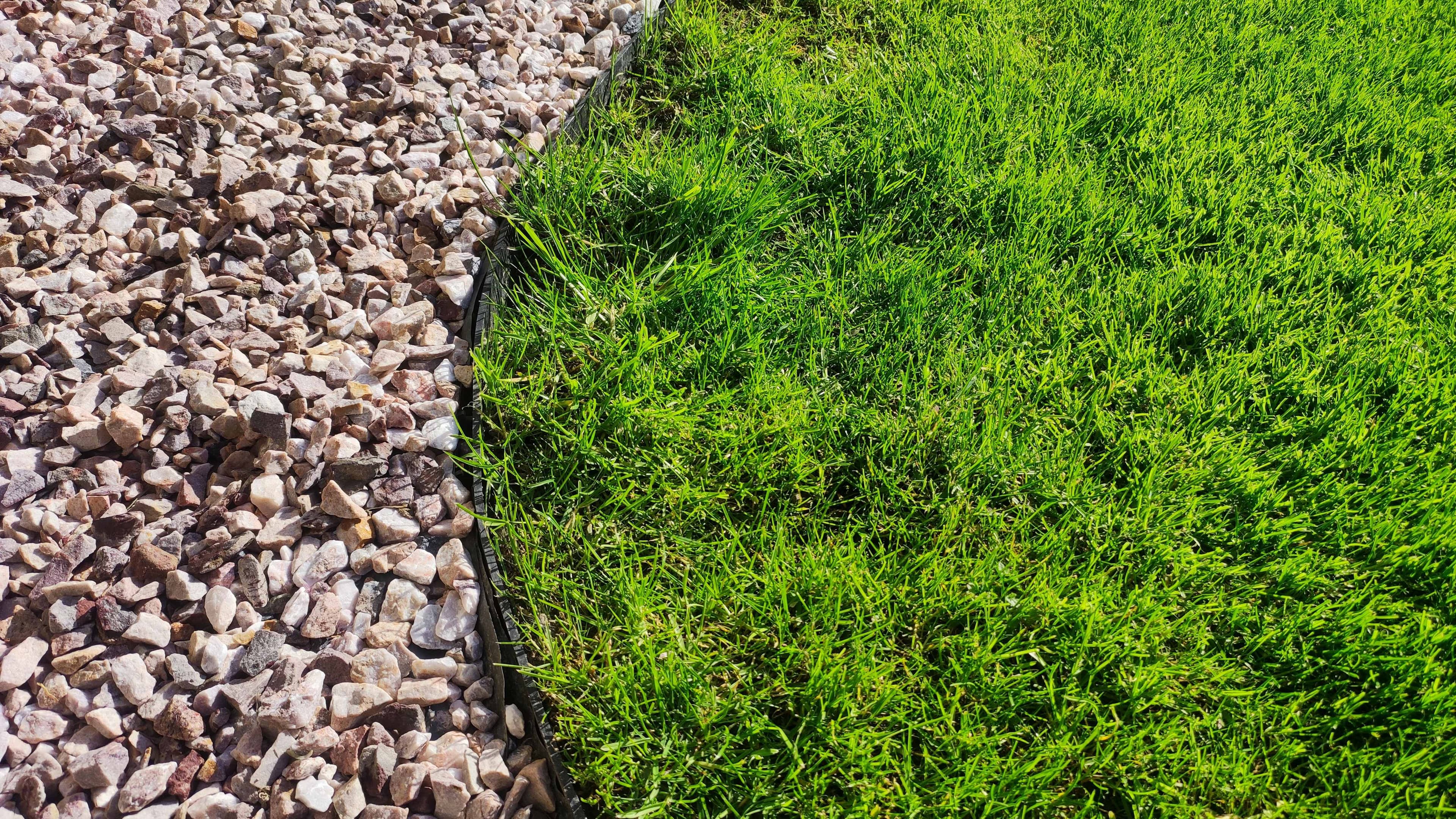 A gravel landscaping bed edge meeting a green lawn with a sprinkler line visible along the border