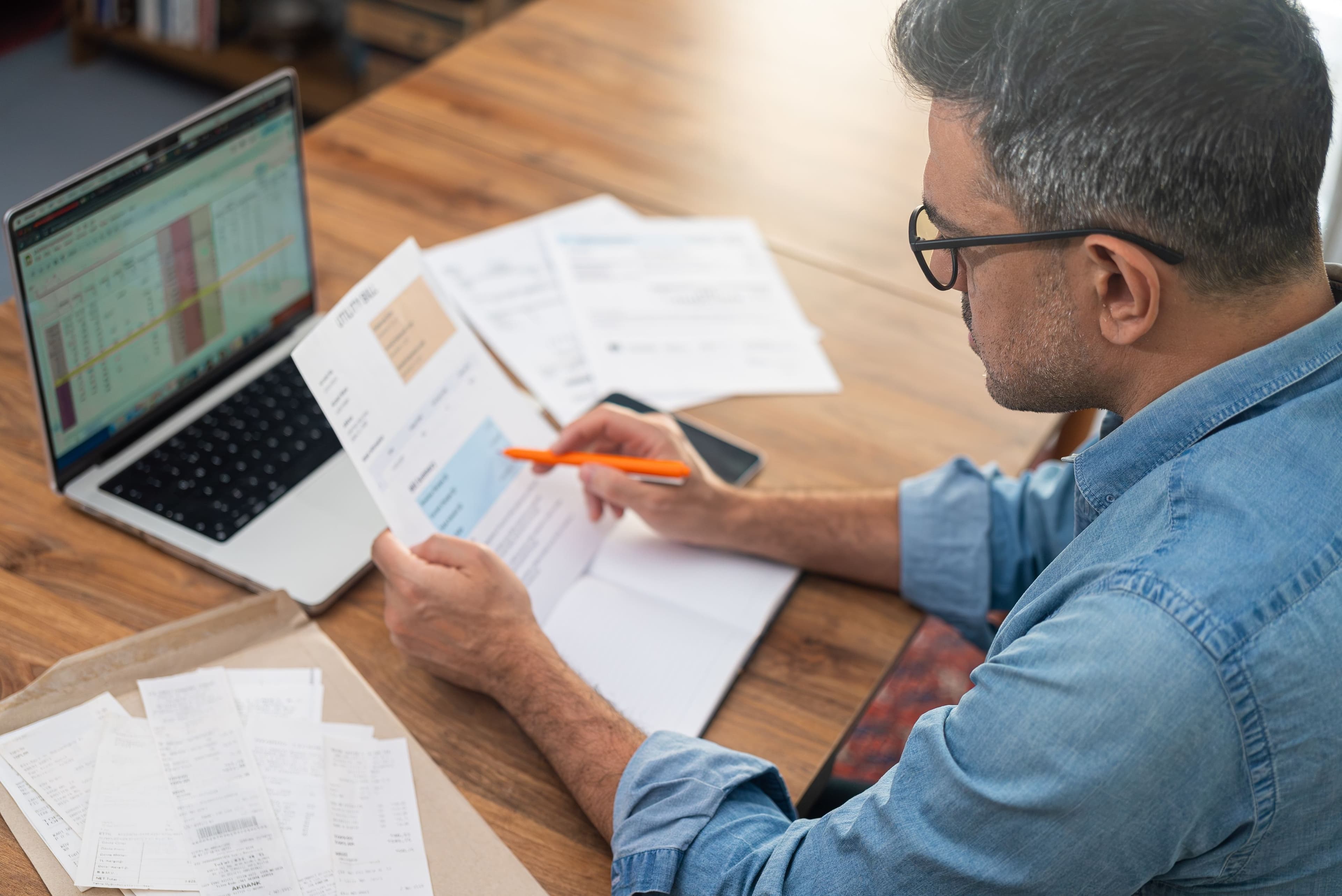 A homeowner reviewing utility bills and receipts at a desk next to an open laptop