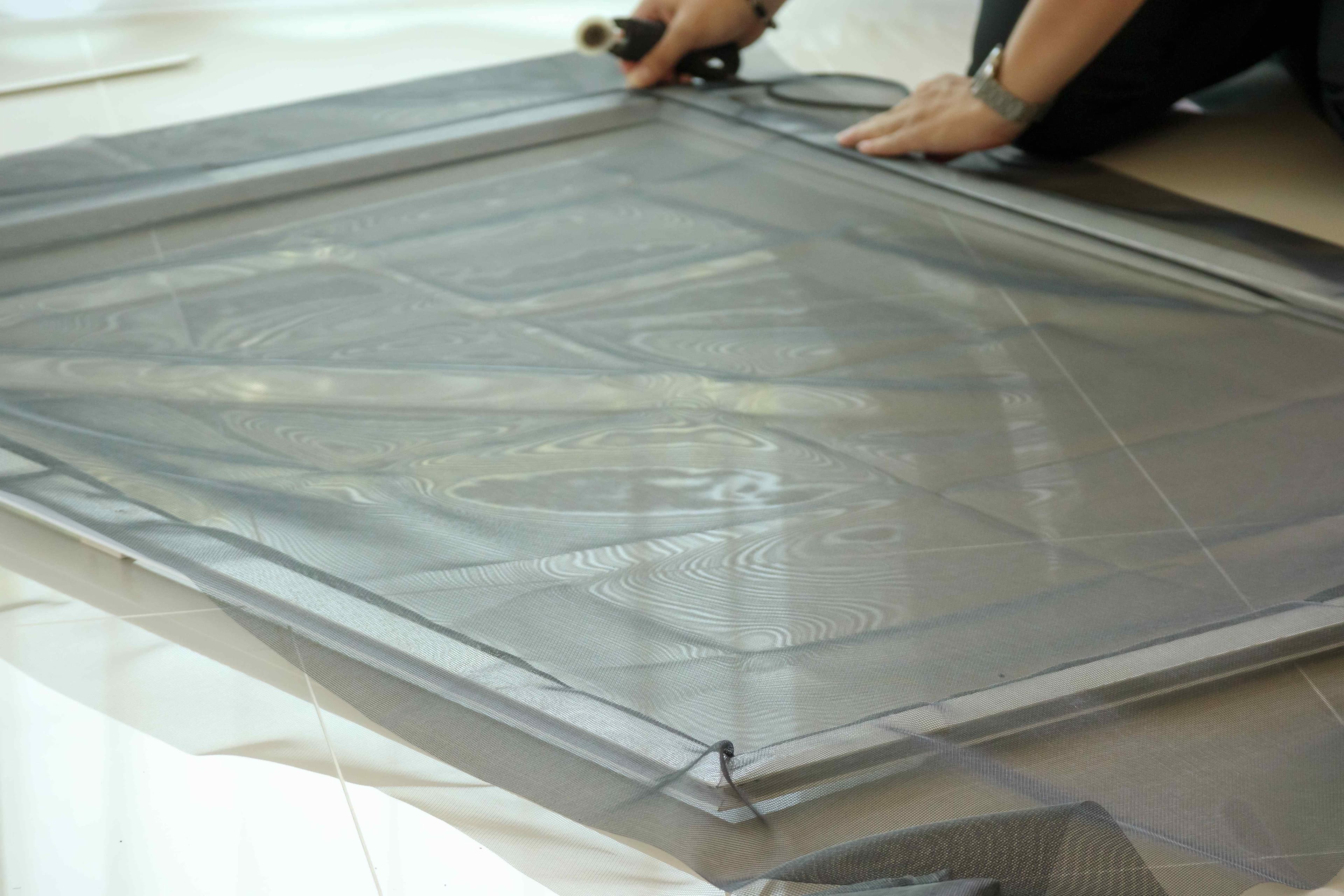 Hands using a roller tool to press new screen mesh and spline into the groove of a screen frame