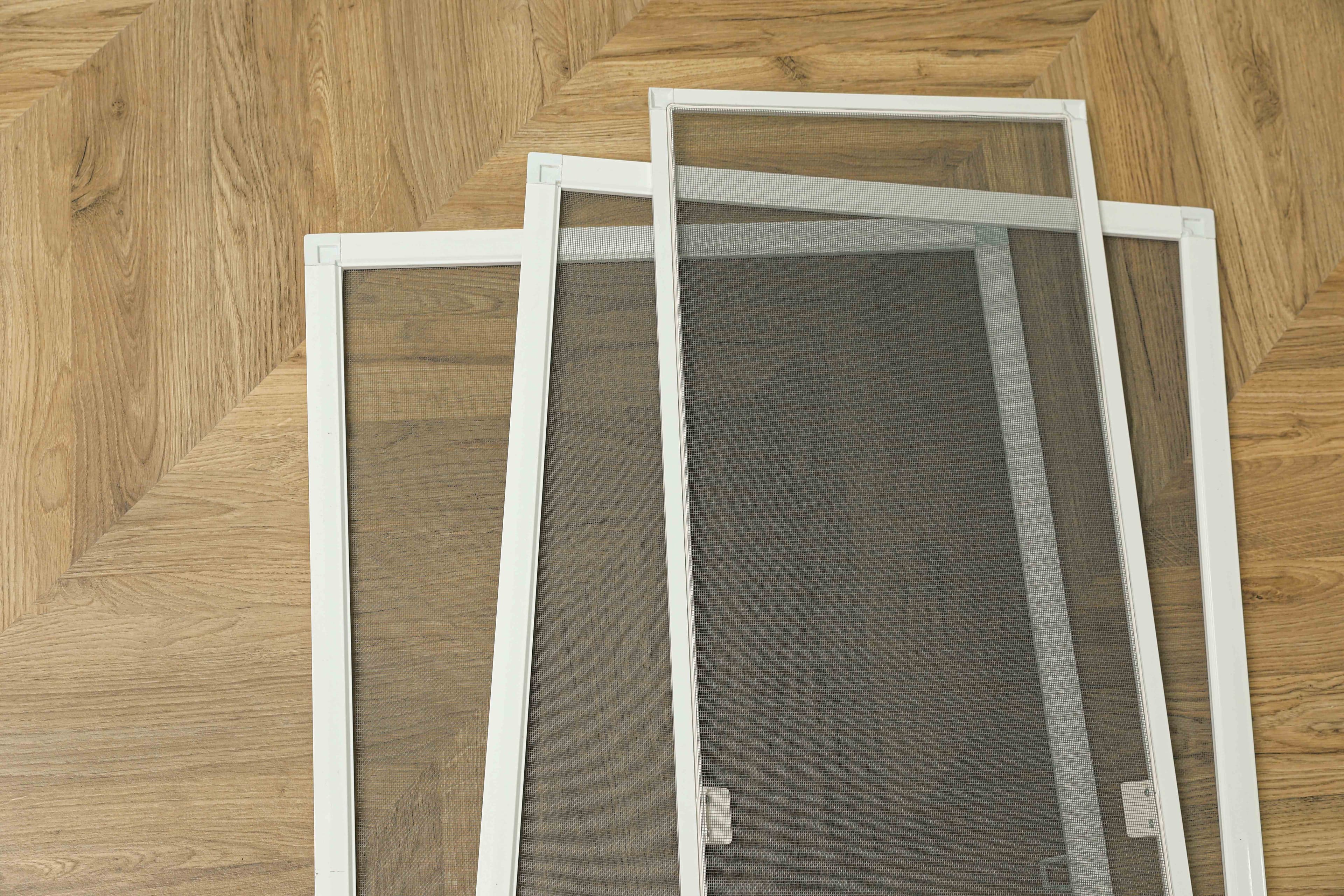 Several removable window screen frames with mesh leaning against a wood floor, showing their aluminum frame construction and corners