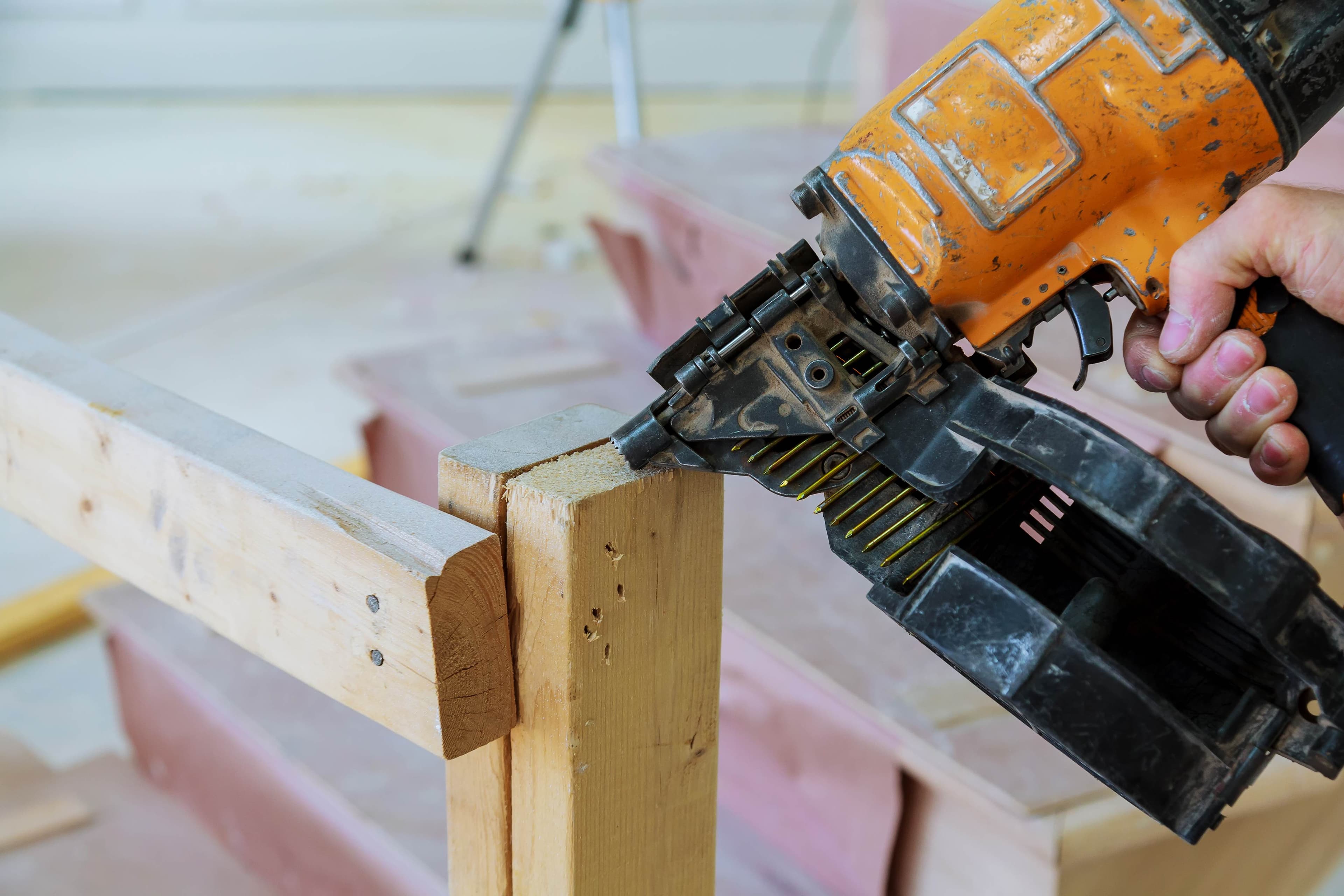 Close-up of a pneumatic nail gun fastening a wood stud during a framing repair