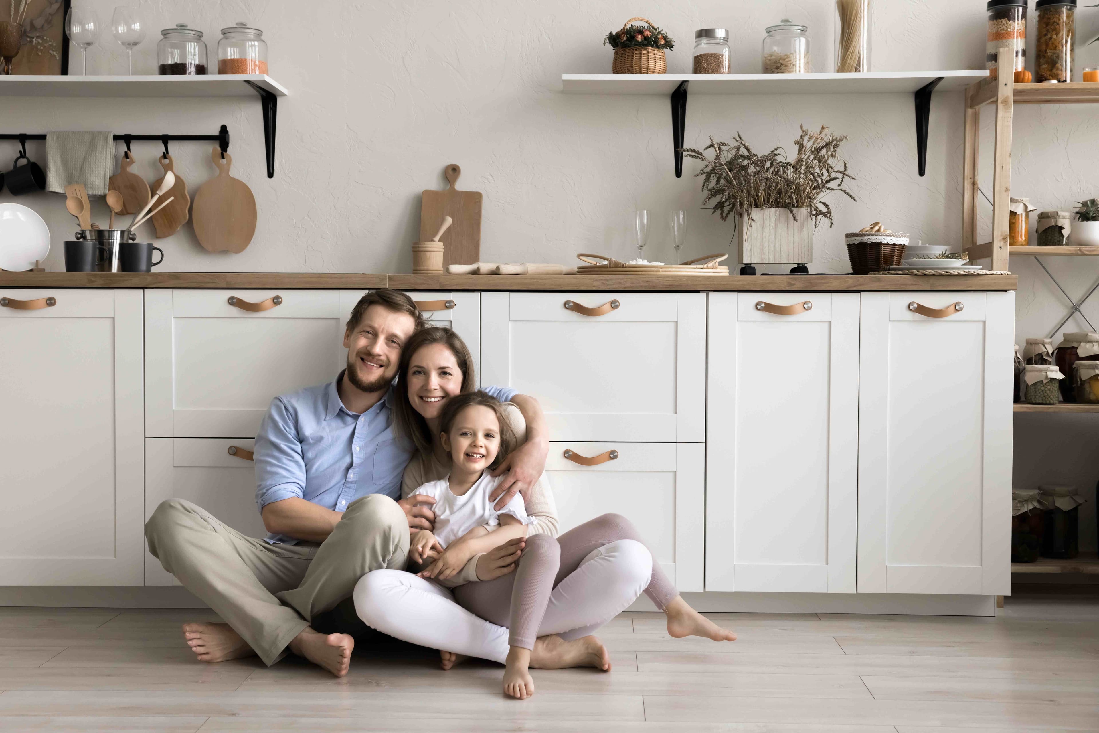 Two adults and a child sitting together on the floor of a home kitchen