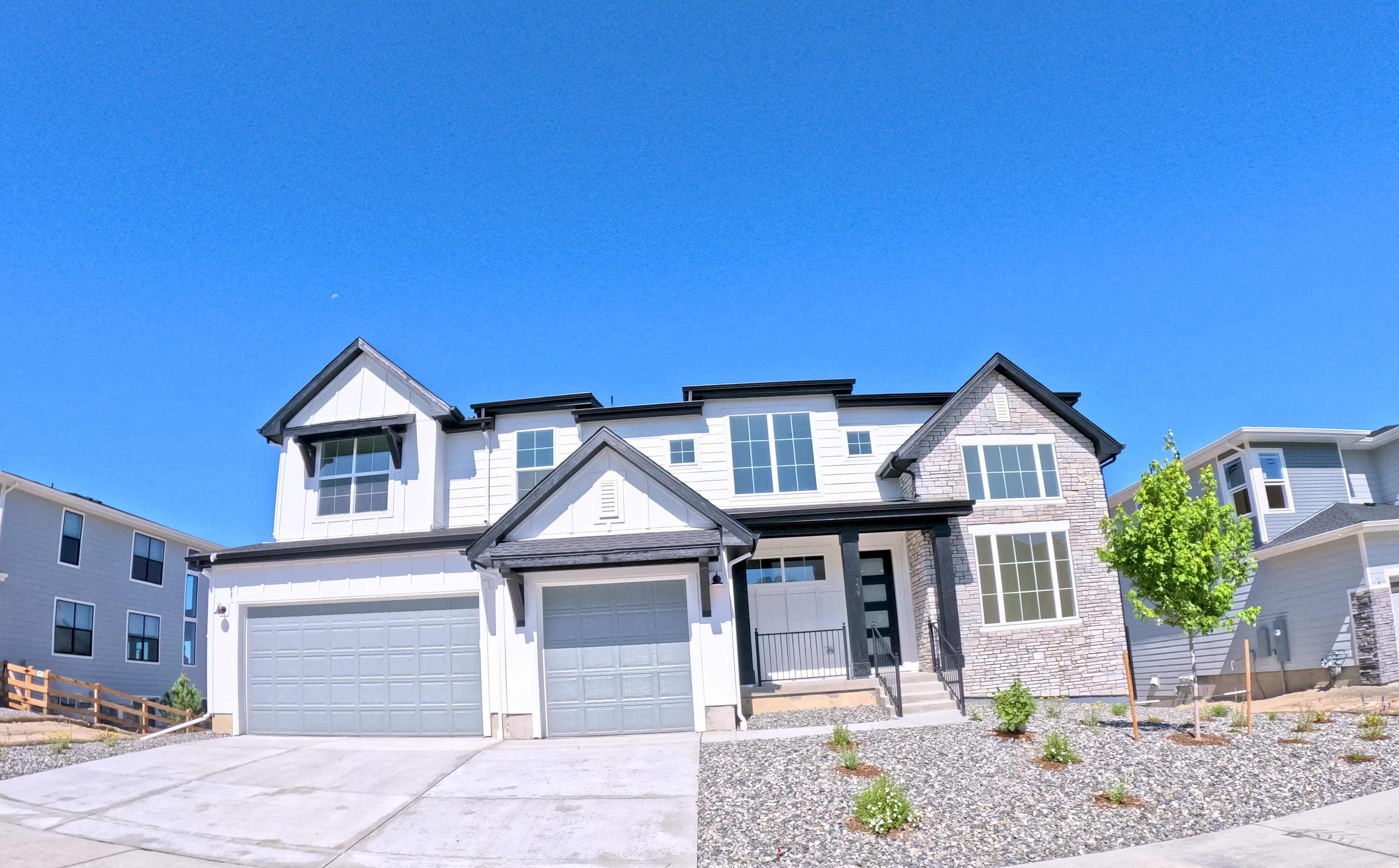 Two-story suburban home exterior with white siding, stone accents, a three-car garage, and a rock-landscaped front yard