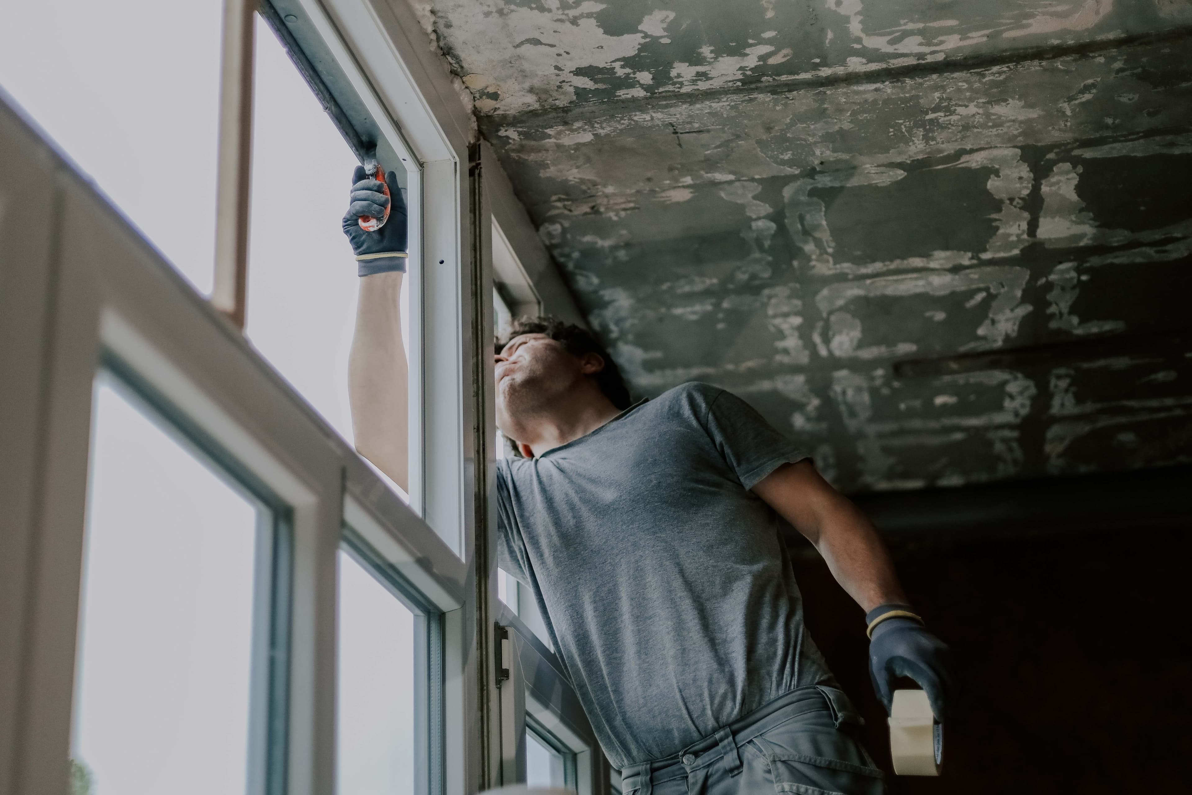 A worker in work gloves prepping a newly installed window during a renovation with a stripped ceiling above