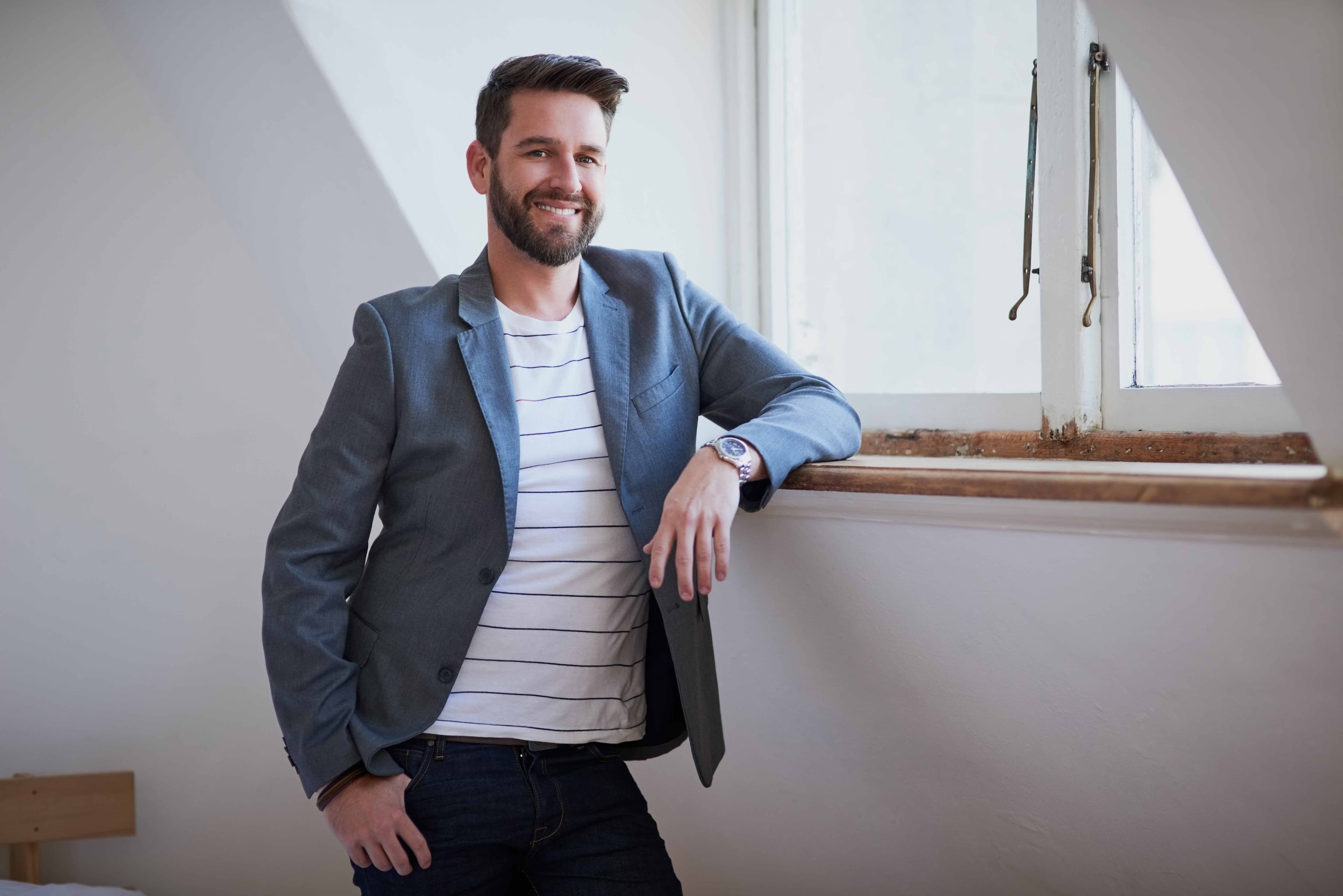 Man leaning against a window sill and smiling in a room with an original wood window frame