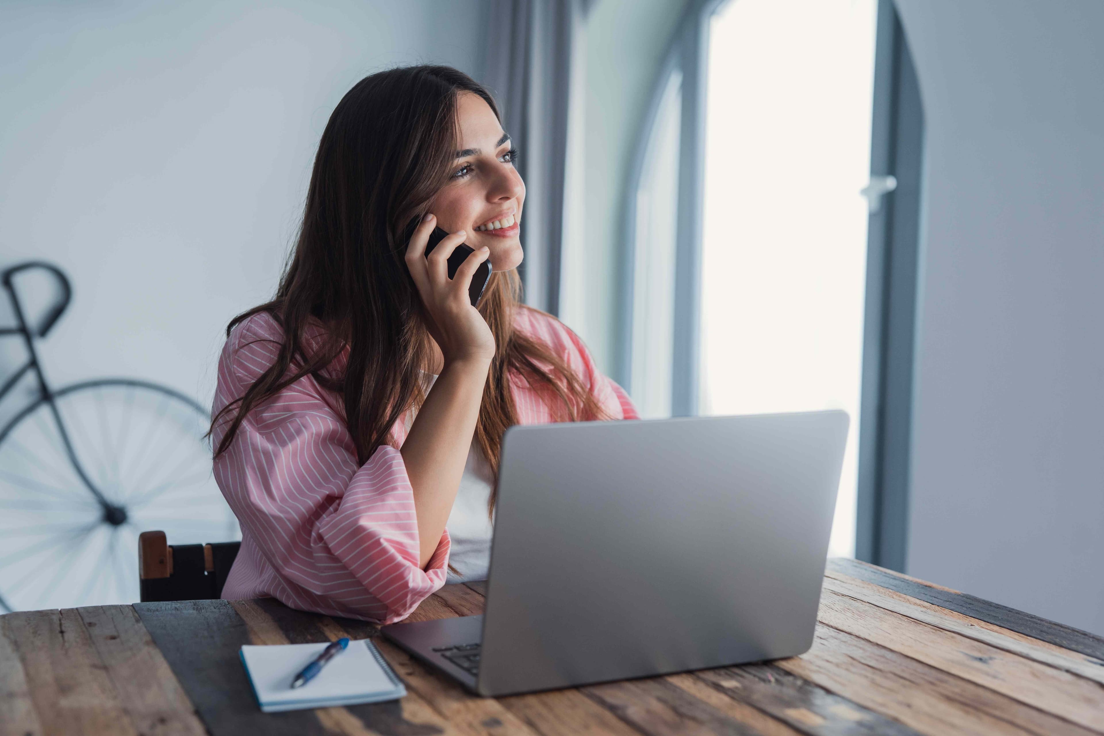 Person smiling while talking on the phone at a desk with an open laptop