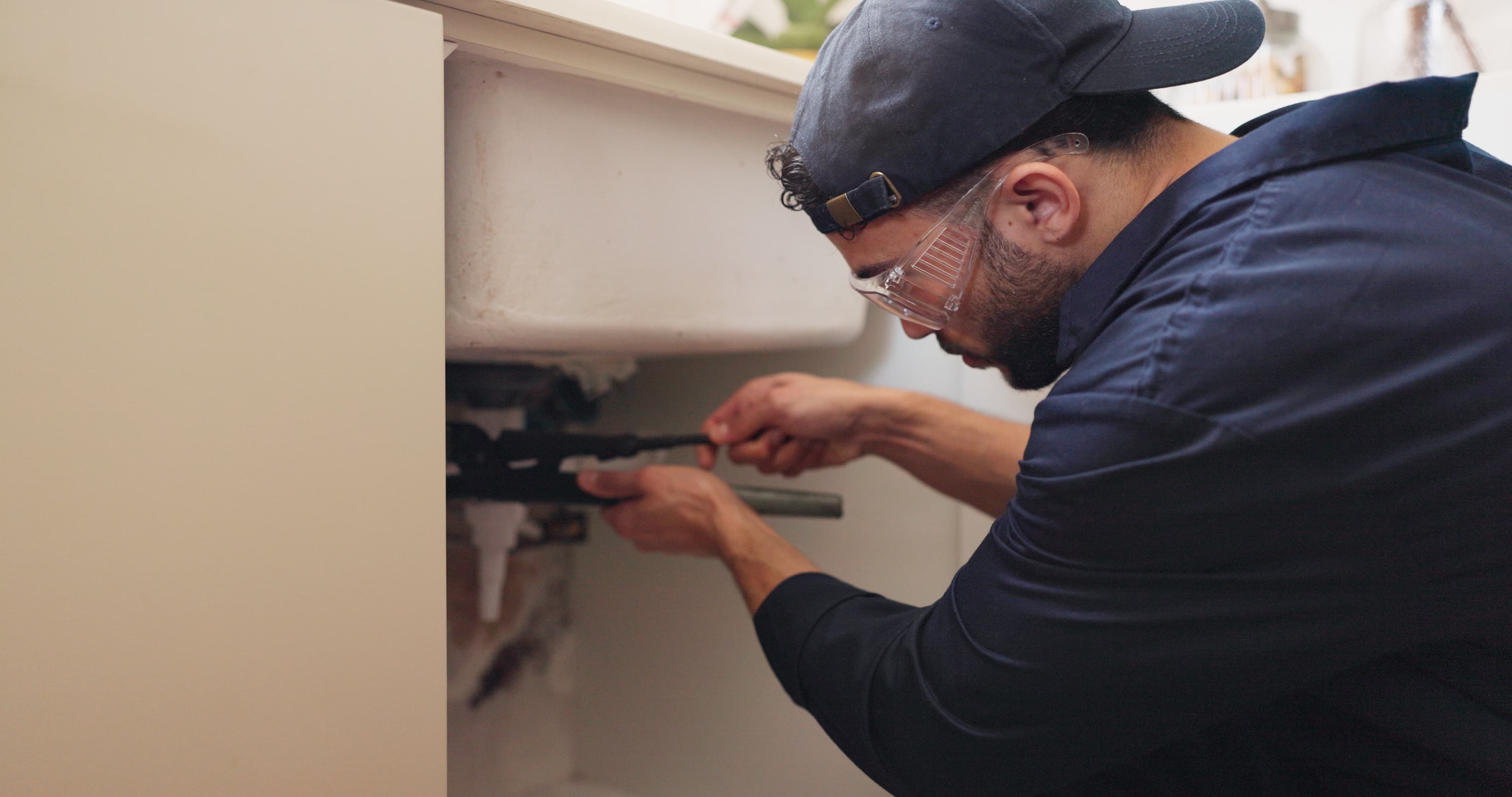 Person using a wrench to work on plumbing pipes underneath a kitchen sink
