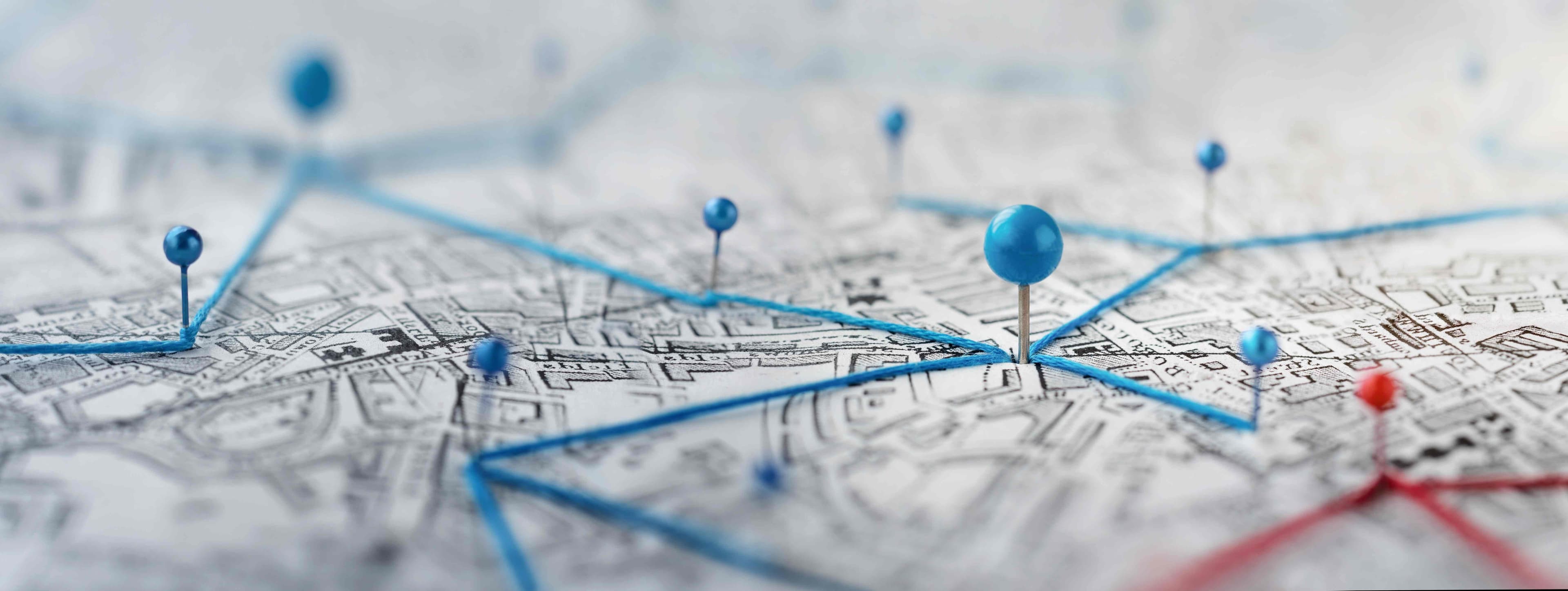 A close-up of a street map marked with blue push-pins connected by thread, representing service coverage across many local communities.