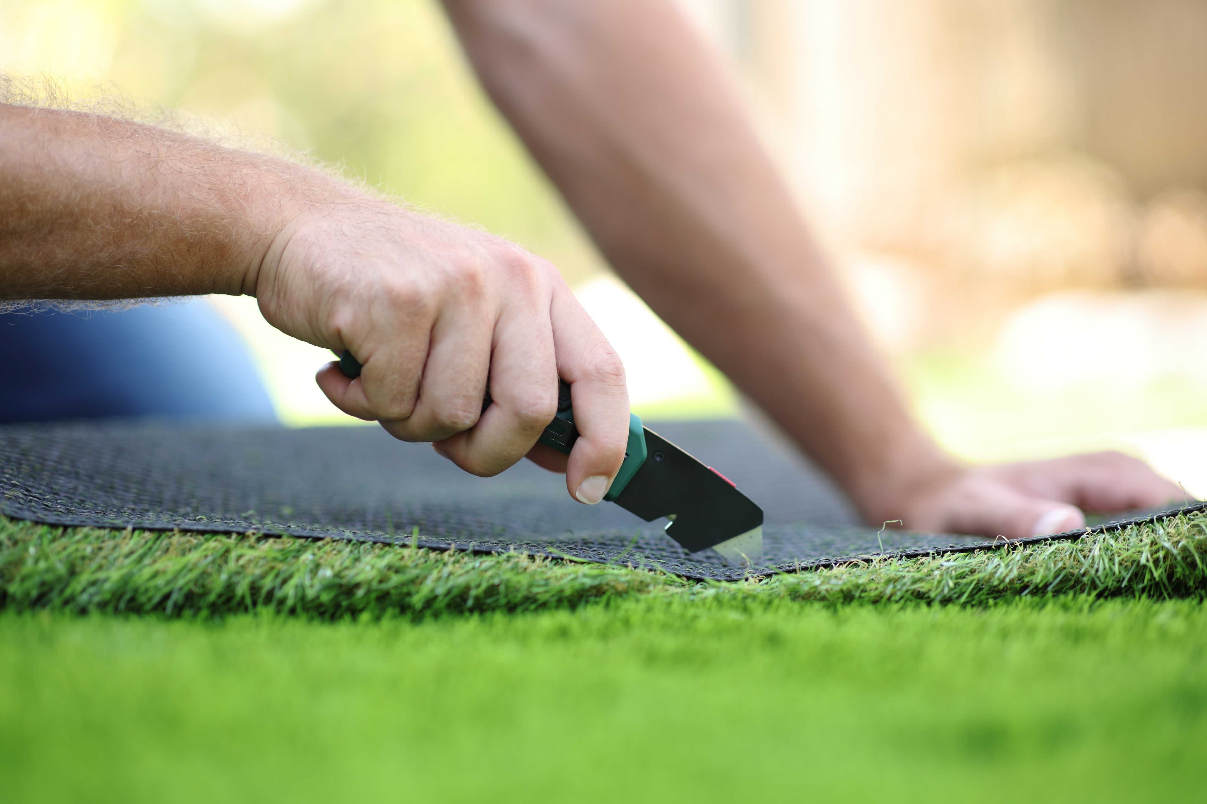 Close-up of hands installing artificial turf edge trim or edging material along green synthetic grass surface