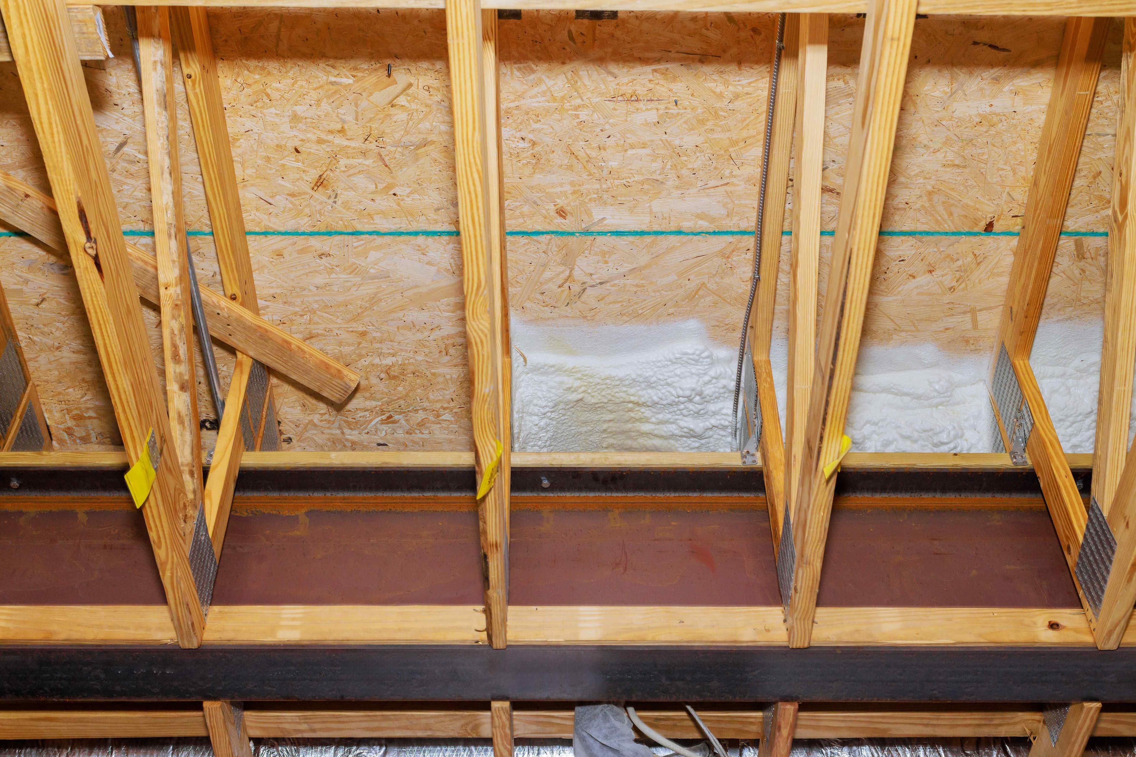 Wood framing against OSB sheathing in an attic space with white spray foam insulation filling the base of the framing bays.