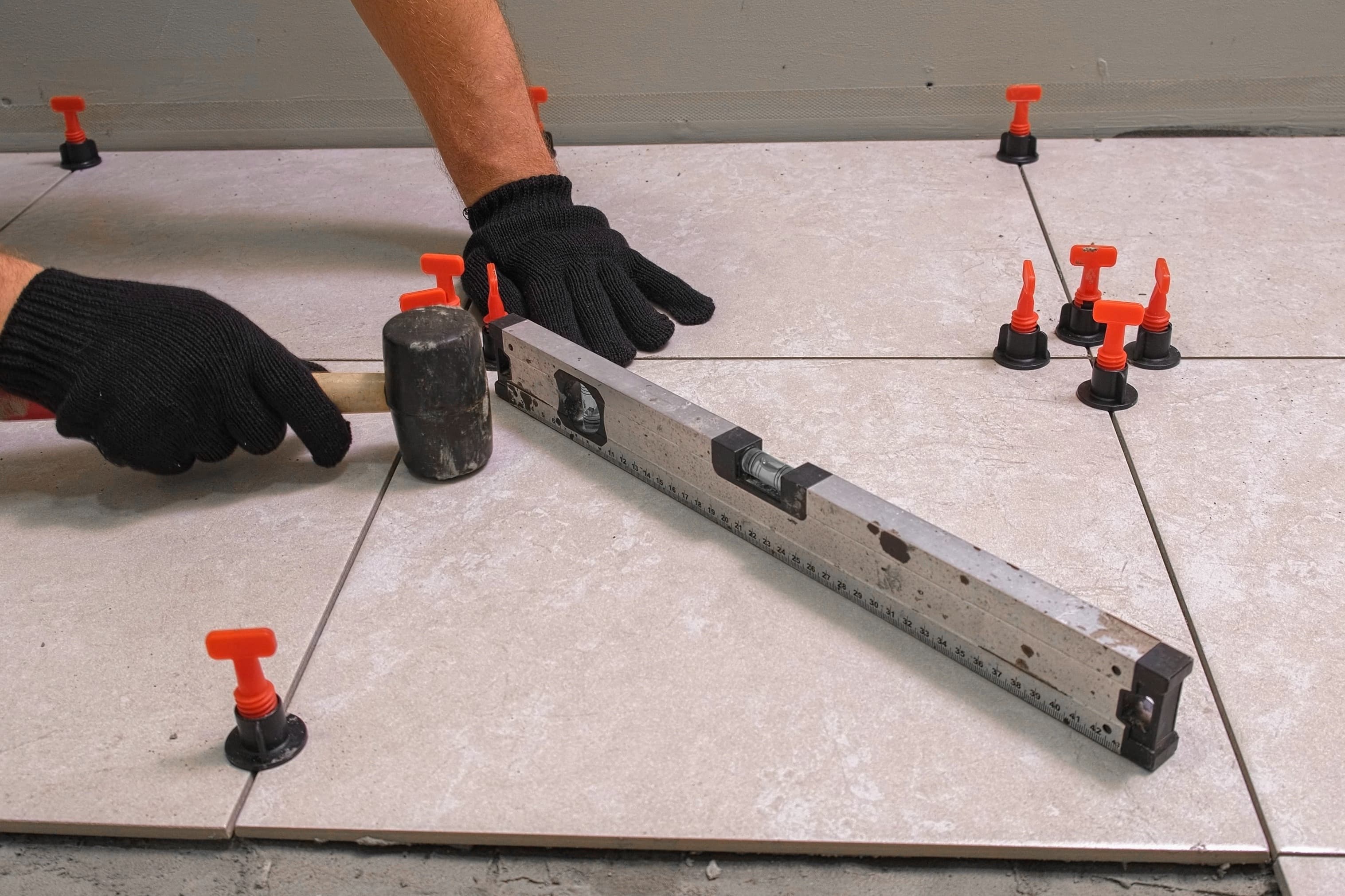 An installer using a rubber mallet and level to set floor tile in place with plastic spacers.