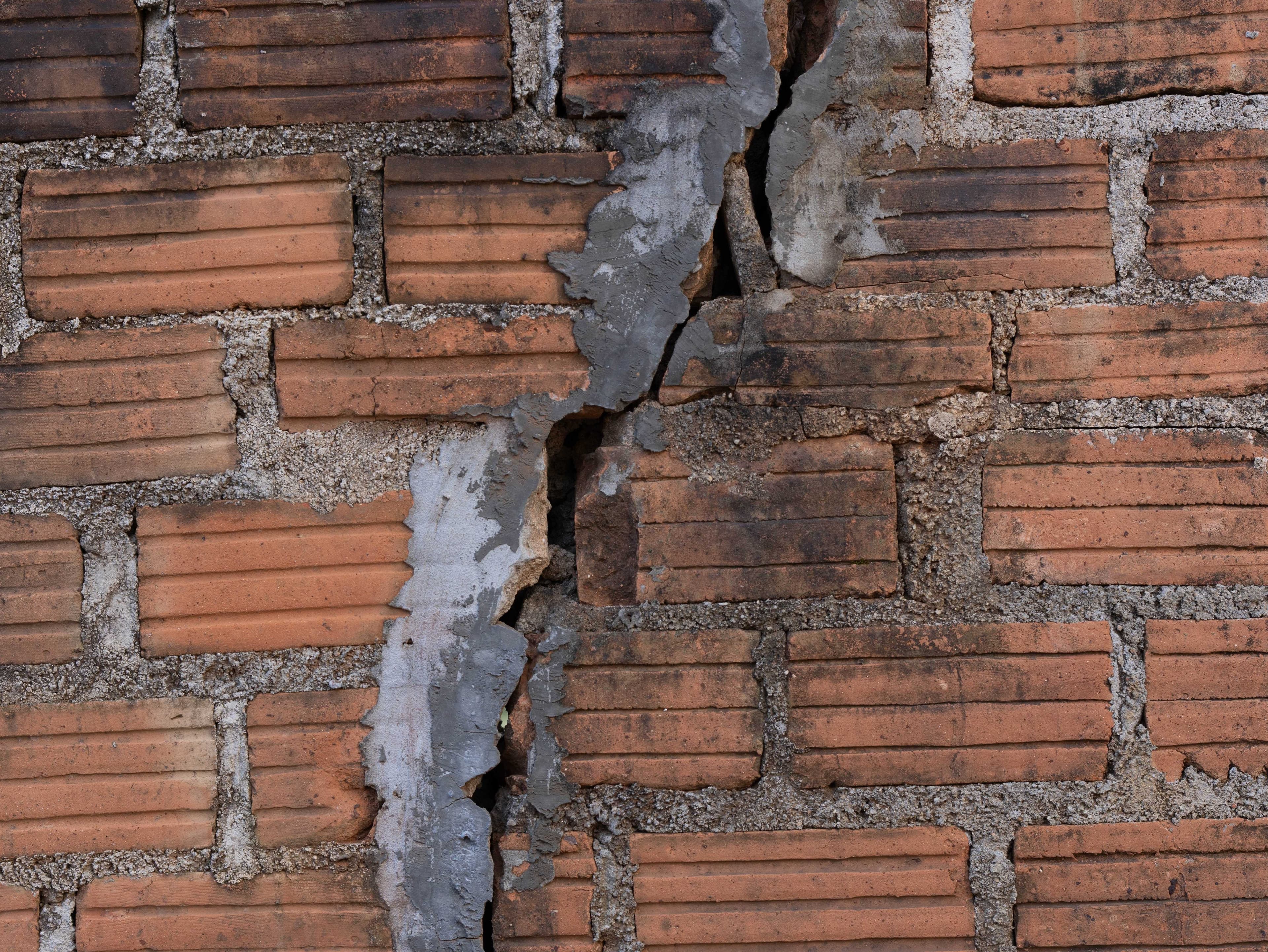 A close-up of a red brick wall with a large diagonal crack running through the bricks and mortar joints.