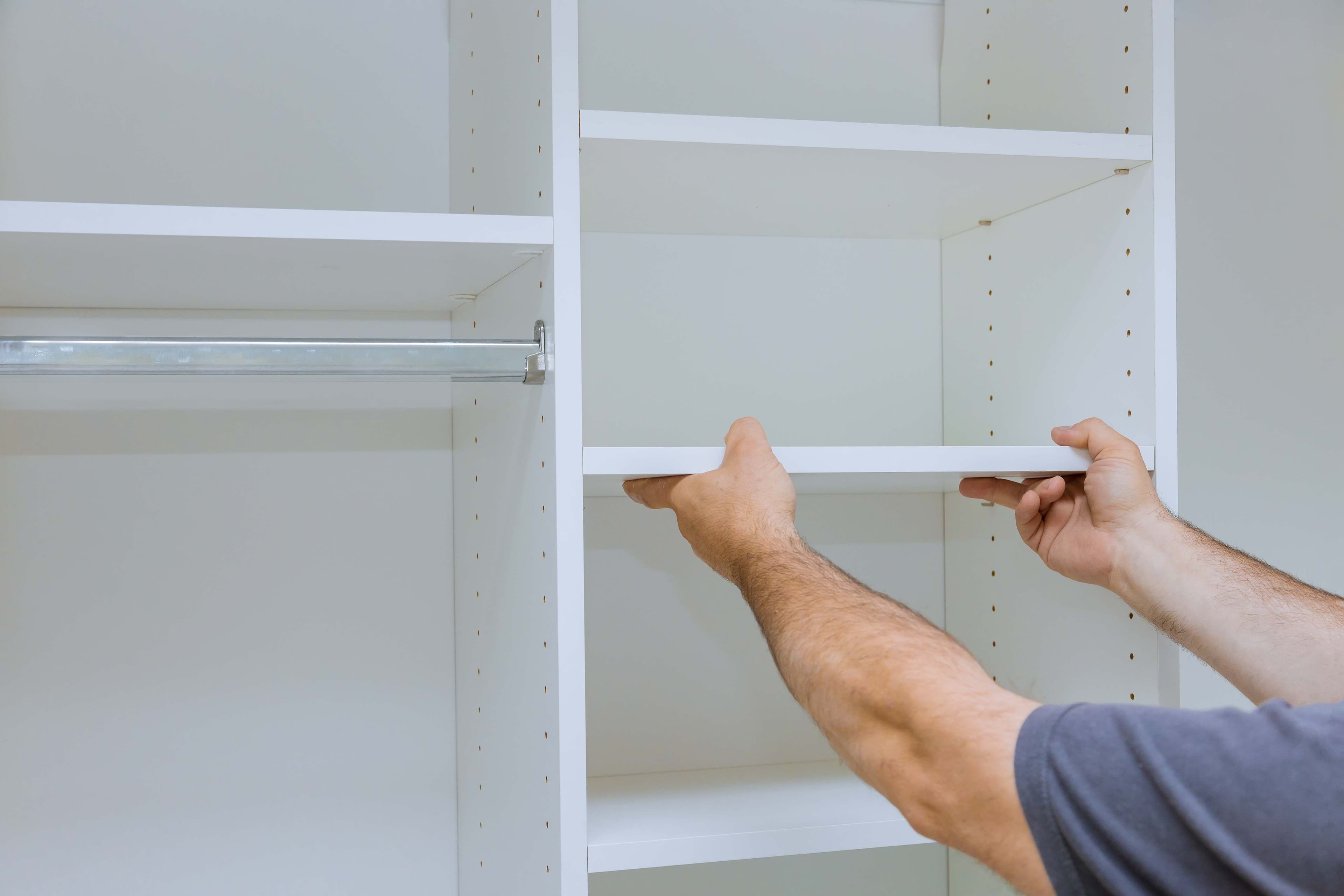 Hands installing a white shelf panel inside a closet storage system