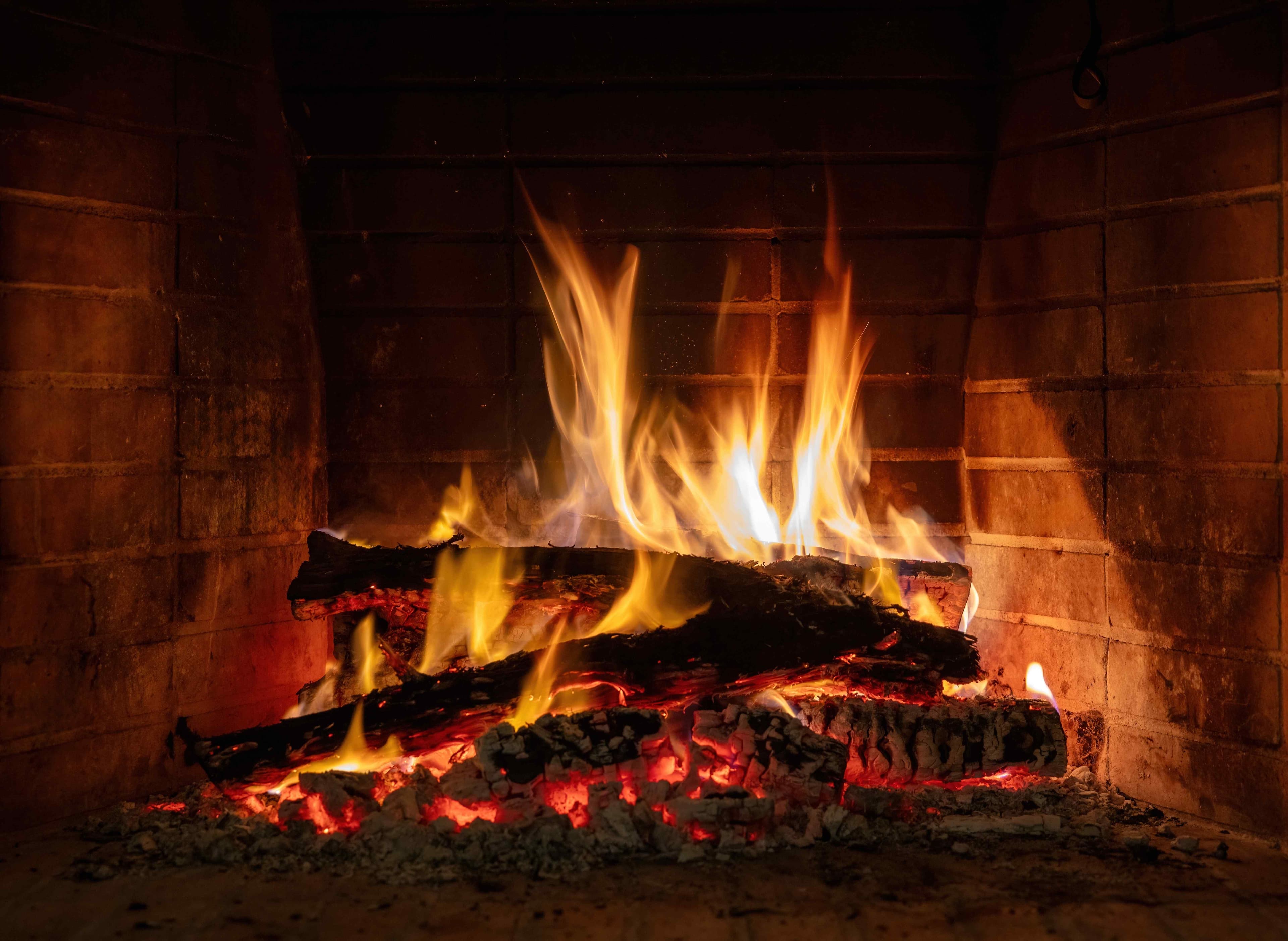 A brick masonry fireplace with a wood fire burning inside, showing the firebox opening where chimney cleaning and maintenance takes place.
