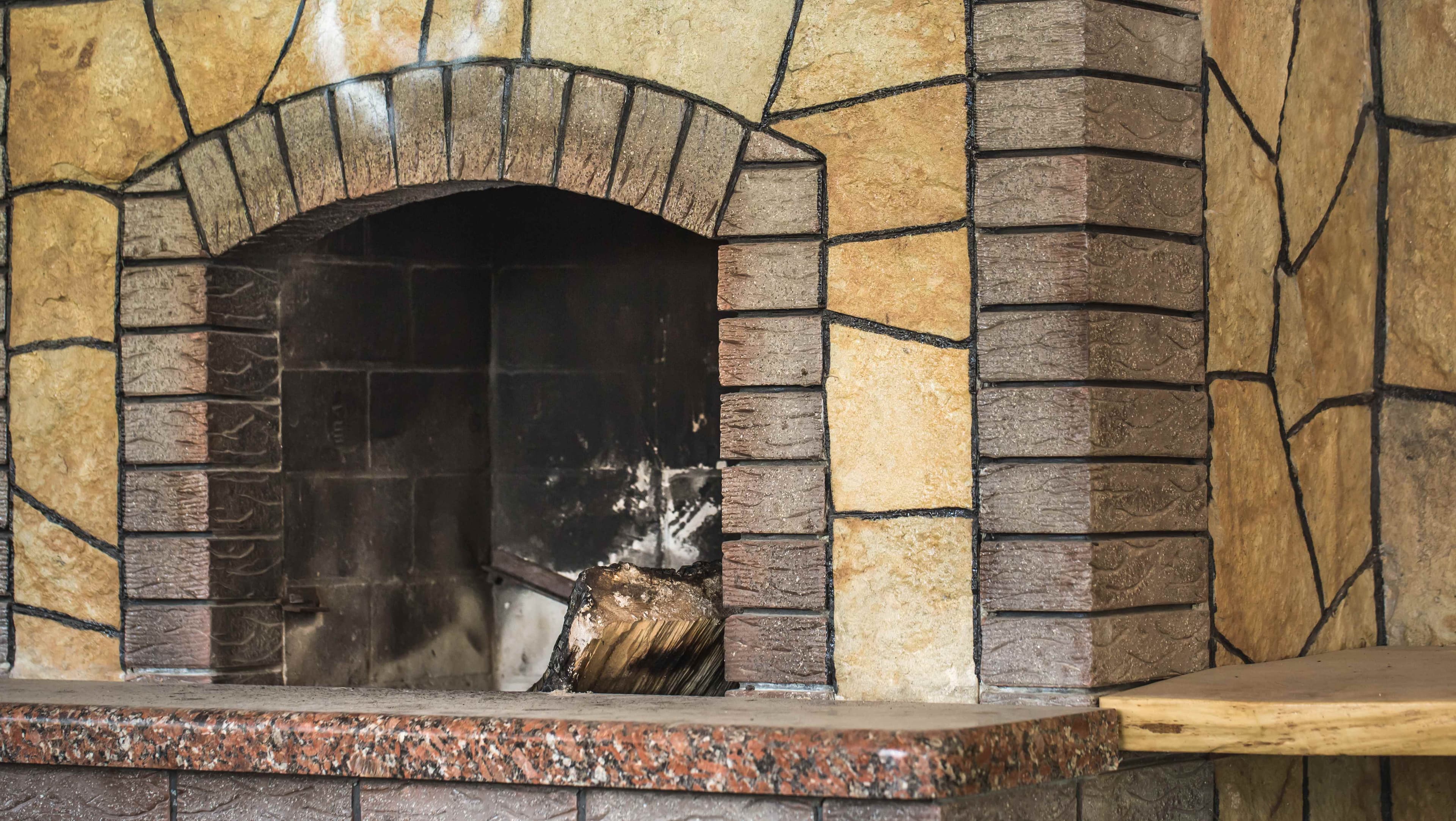 A stone fireplace opening with visible soot staining inside the firebox and a partially burnt log resting near the hearth.