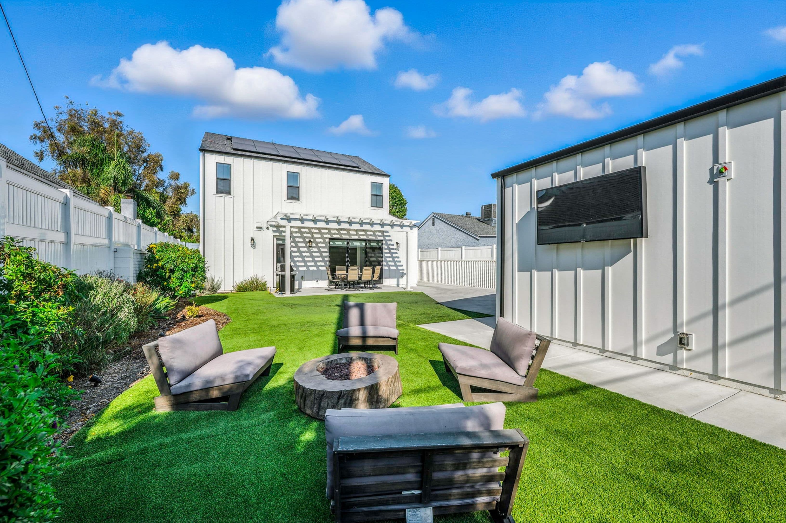 A backyard with a finished concrete patio near the house and a concrete walkway running along the side past a seating area.