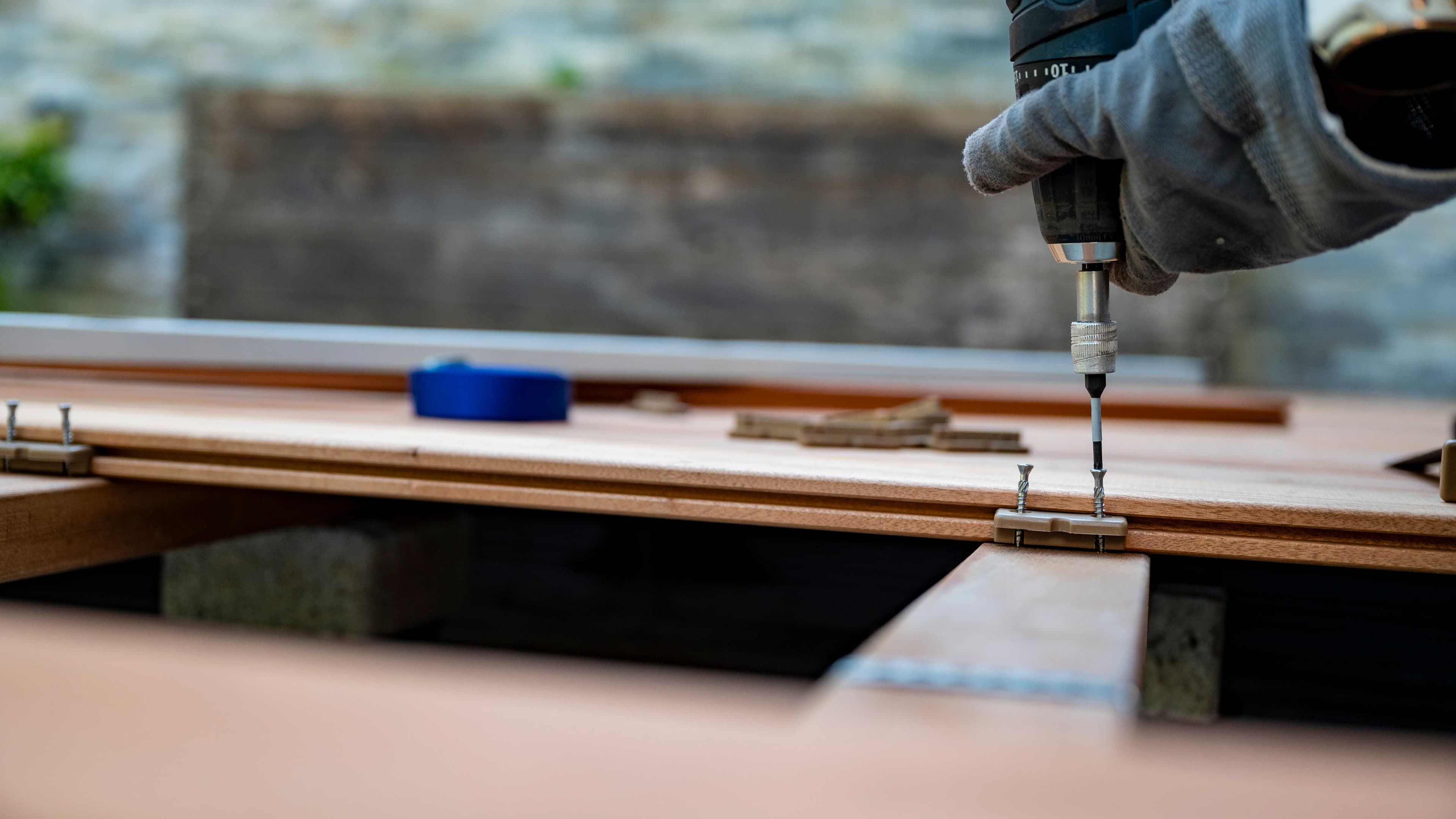 Gloved hand securing a deck board with a drill