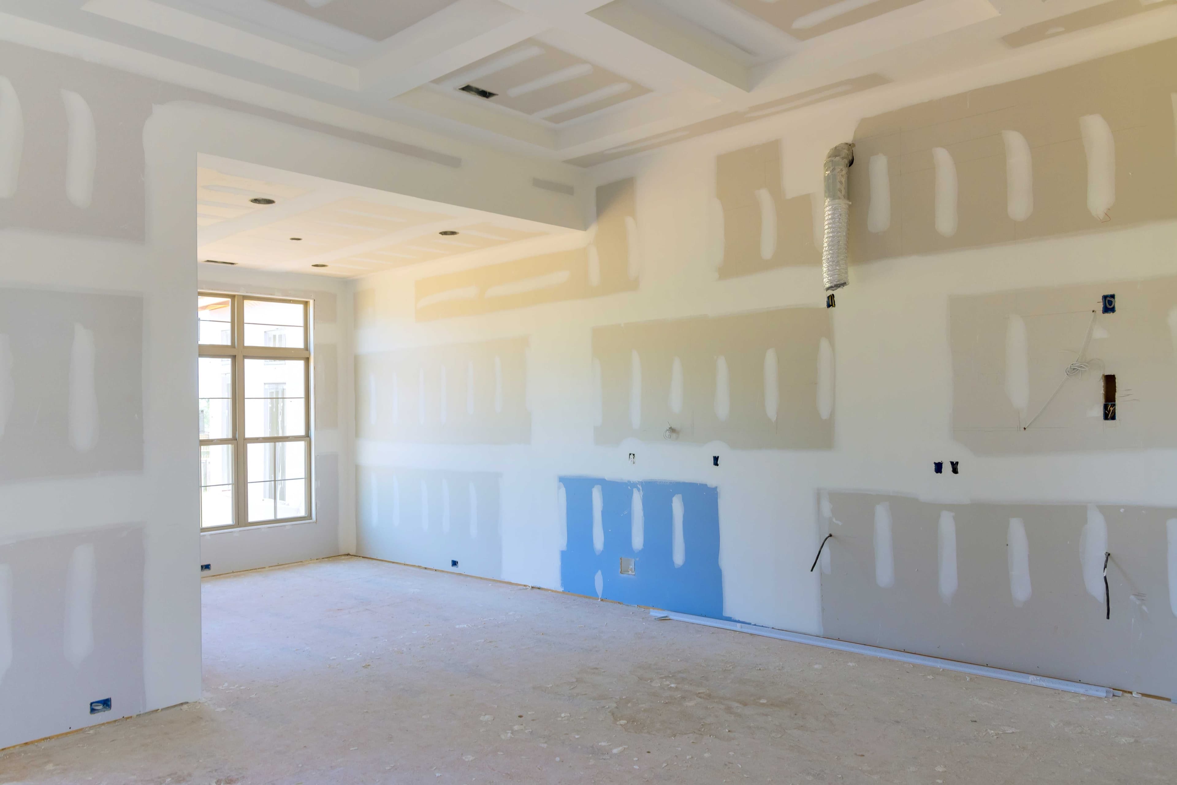An unfinished room with drywall installed, showing a patched section with different colored joint compound blending into the surrounding wall.