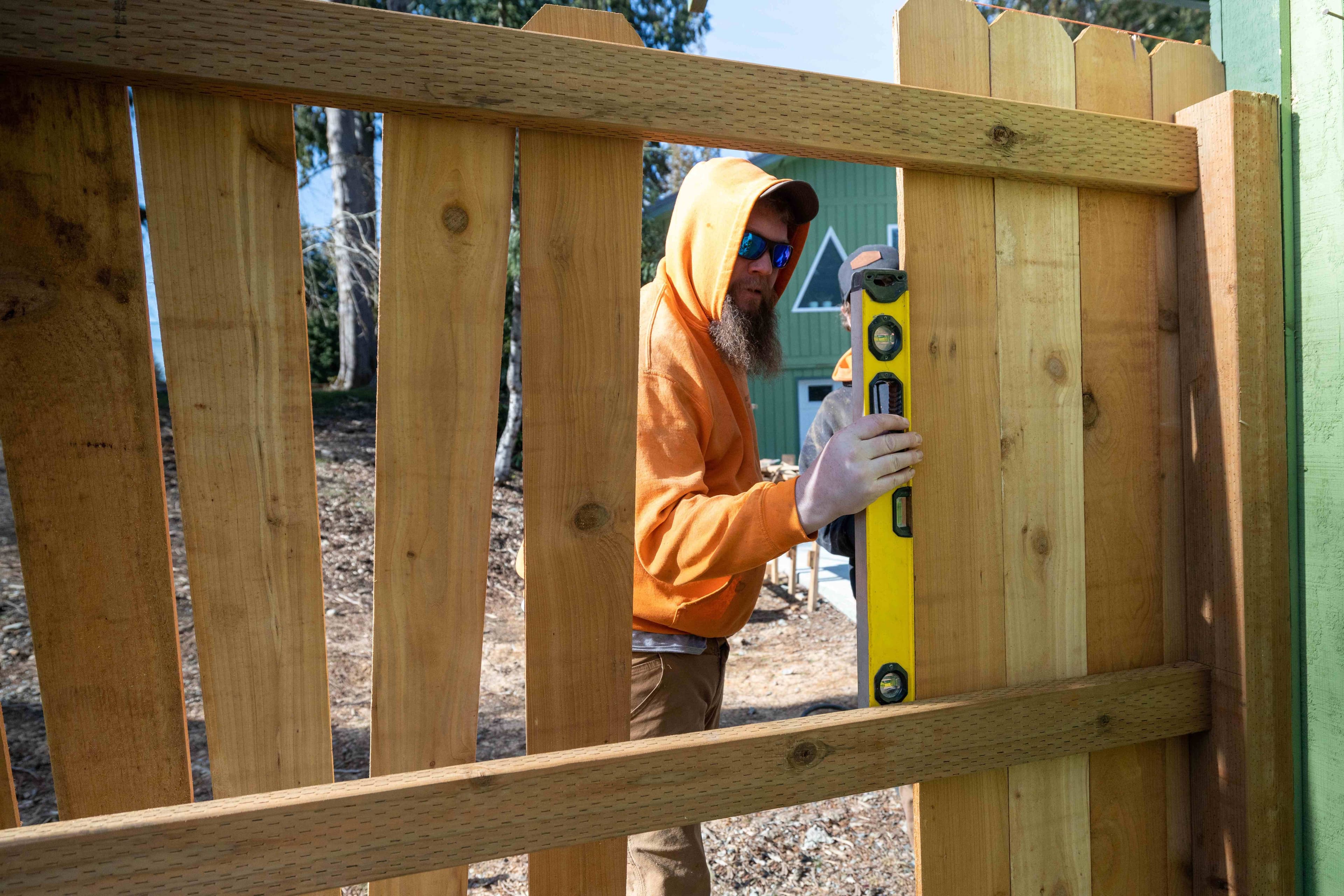 Two people using a level to check the alignment of a wood picket gate during fence gate installation.