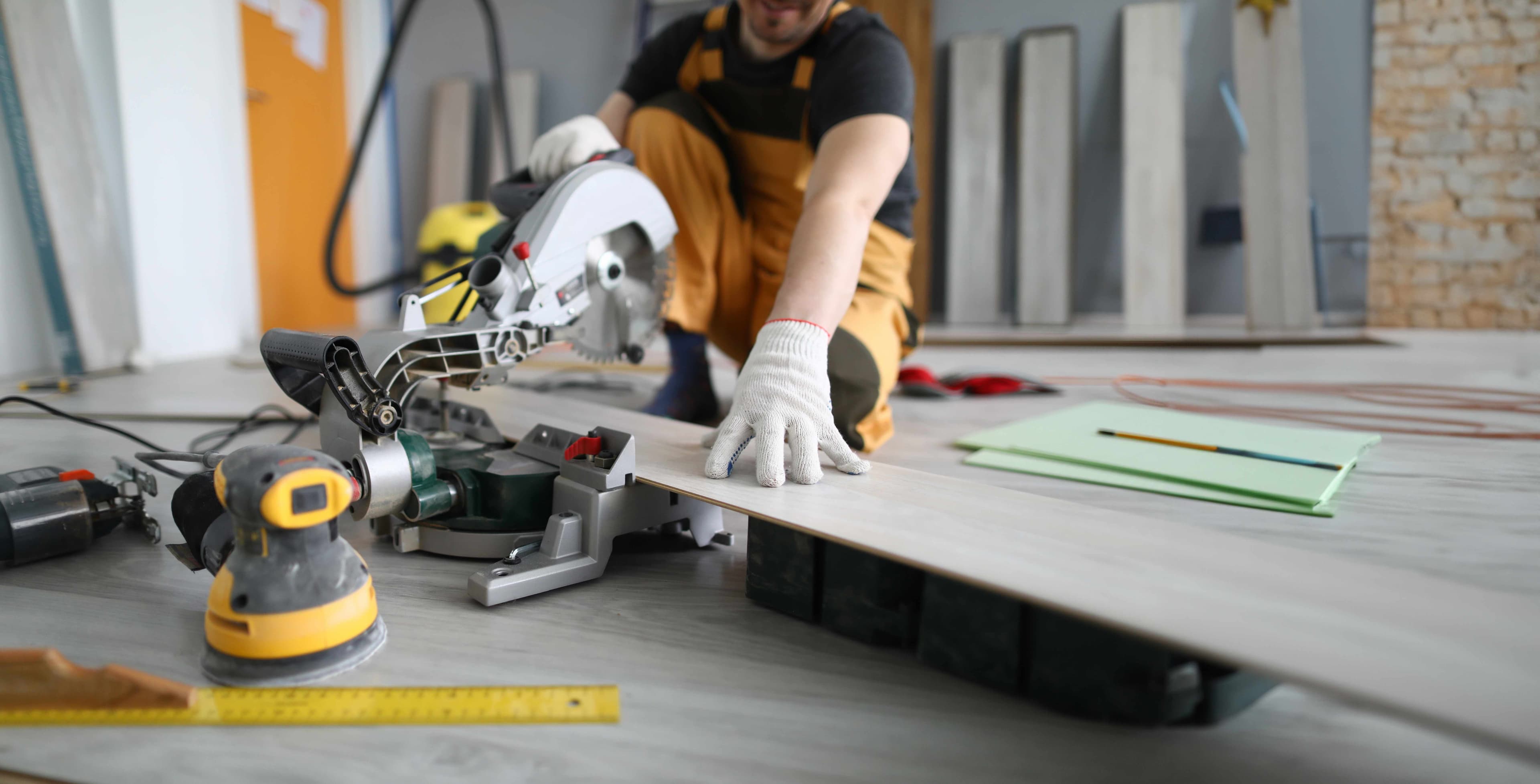 An installer using a miter saw and sander to cut a plank of wood-look flooring before fitting it into place.