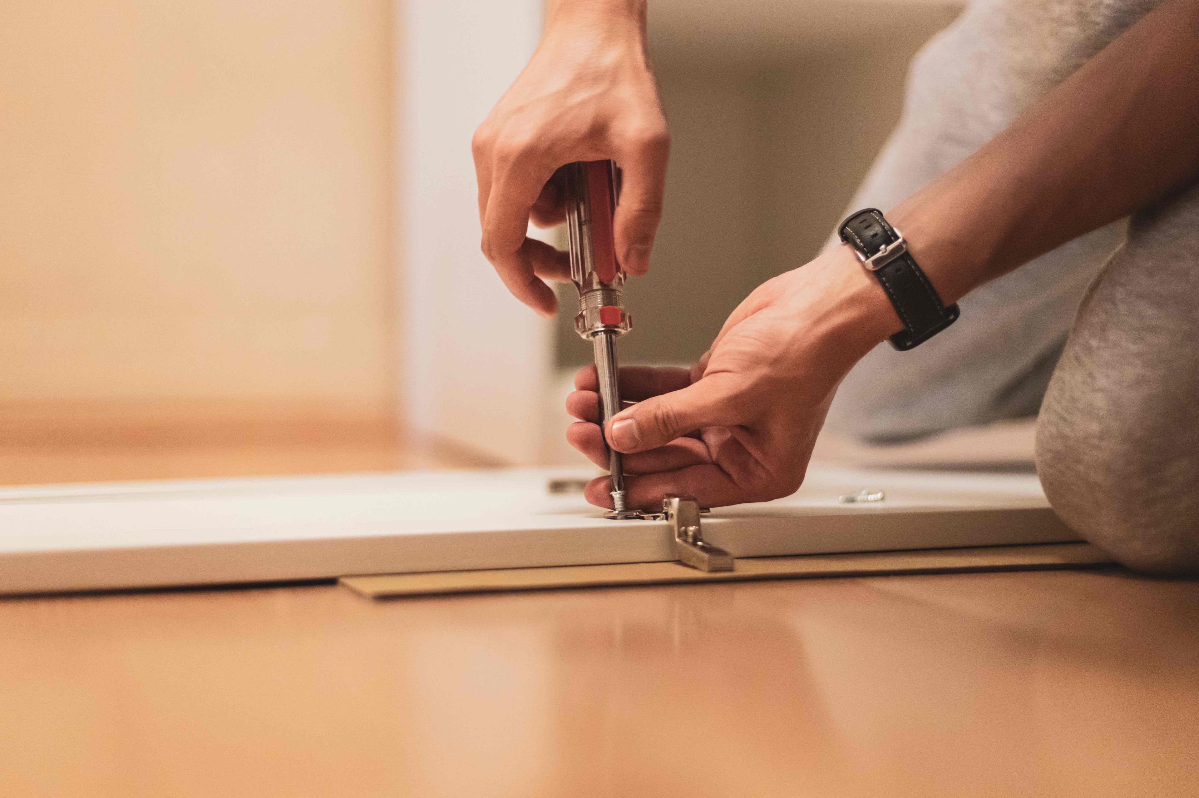 Two hands using screwdriver to install or adjust cabinet door hinge hardware