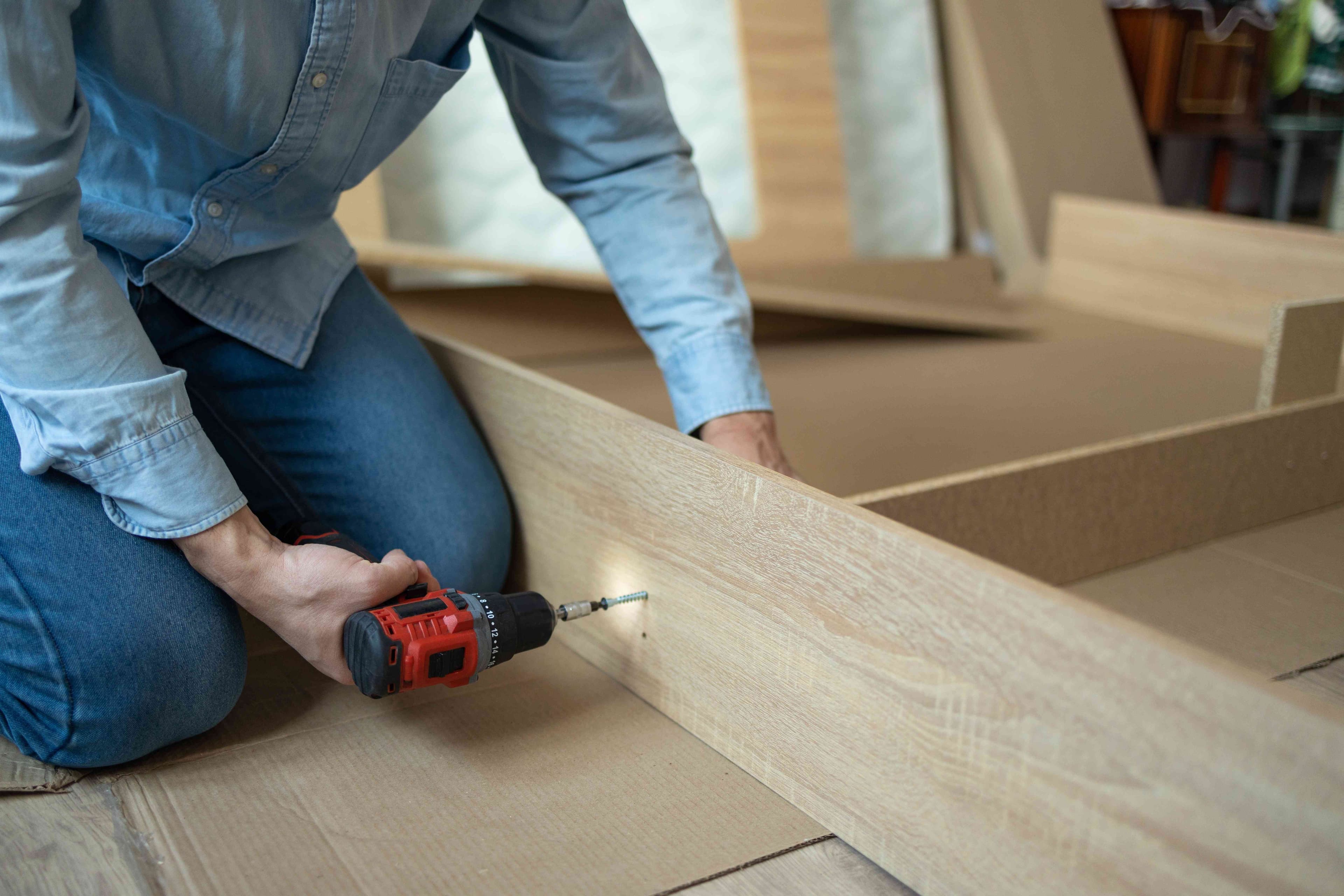 Person drilling into a wooden shelf component during furniture assembly