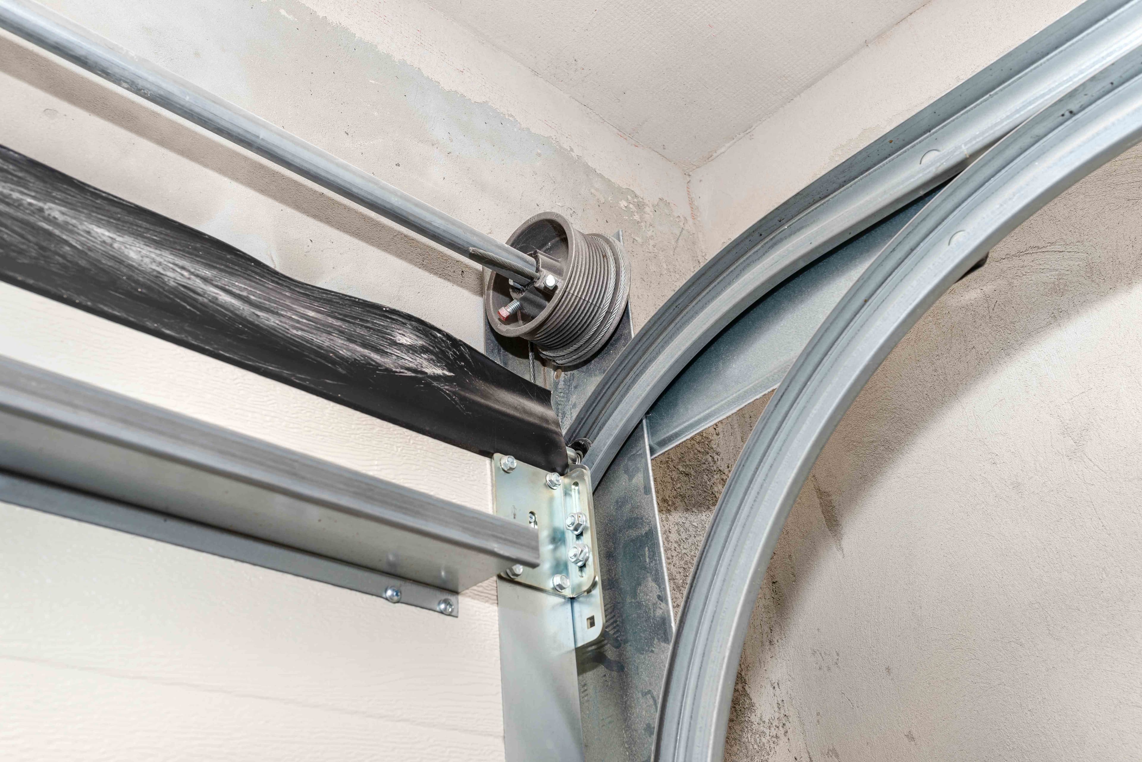 A garage door torsion spring, cable, and mounting bracket installed near the top corner of the track.