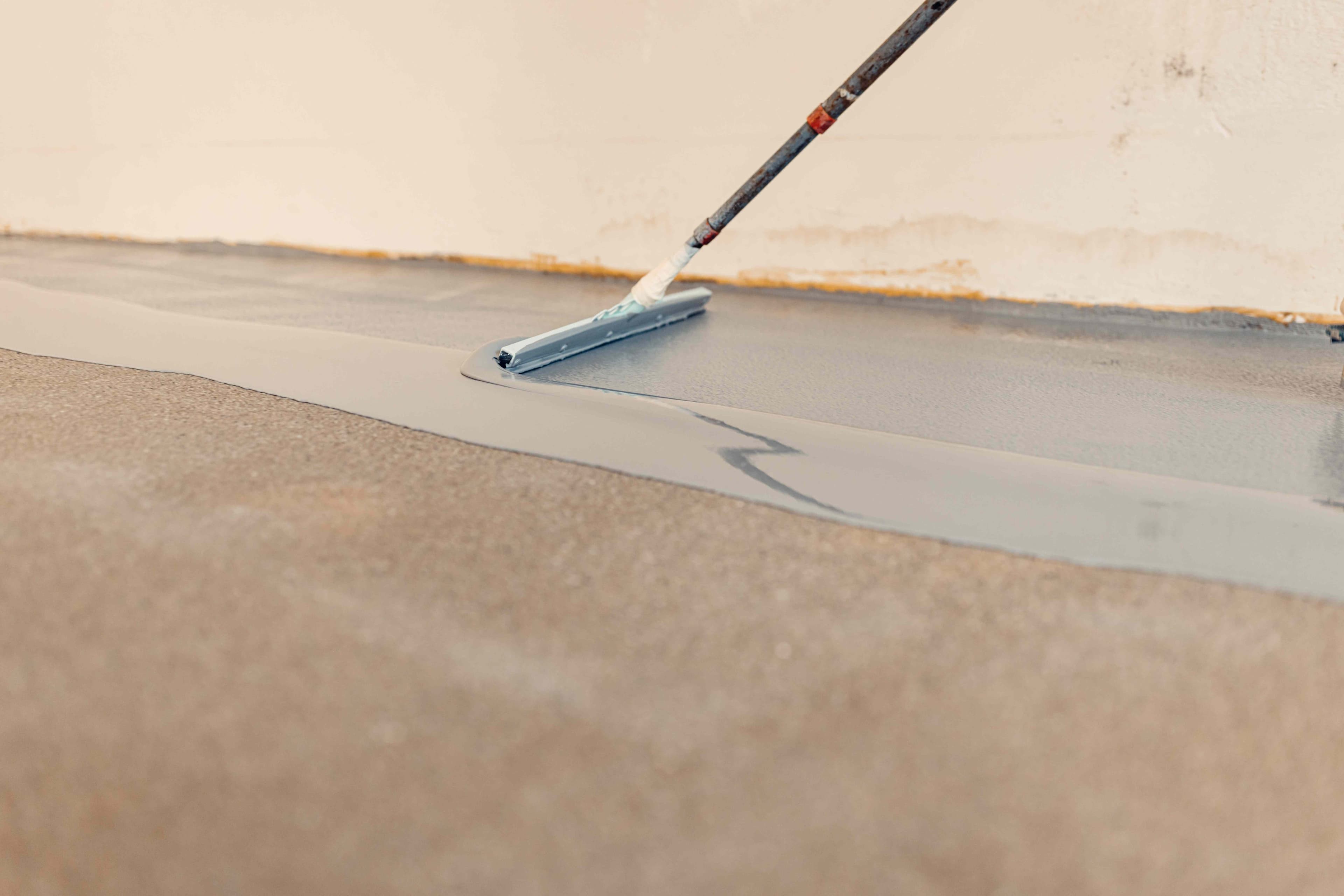 Gray epoxy coating being spread with a squeegee along a garage wall edge