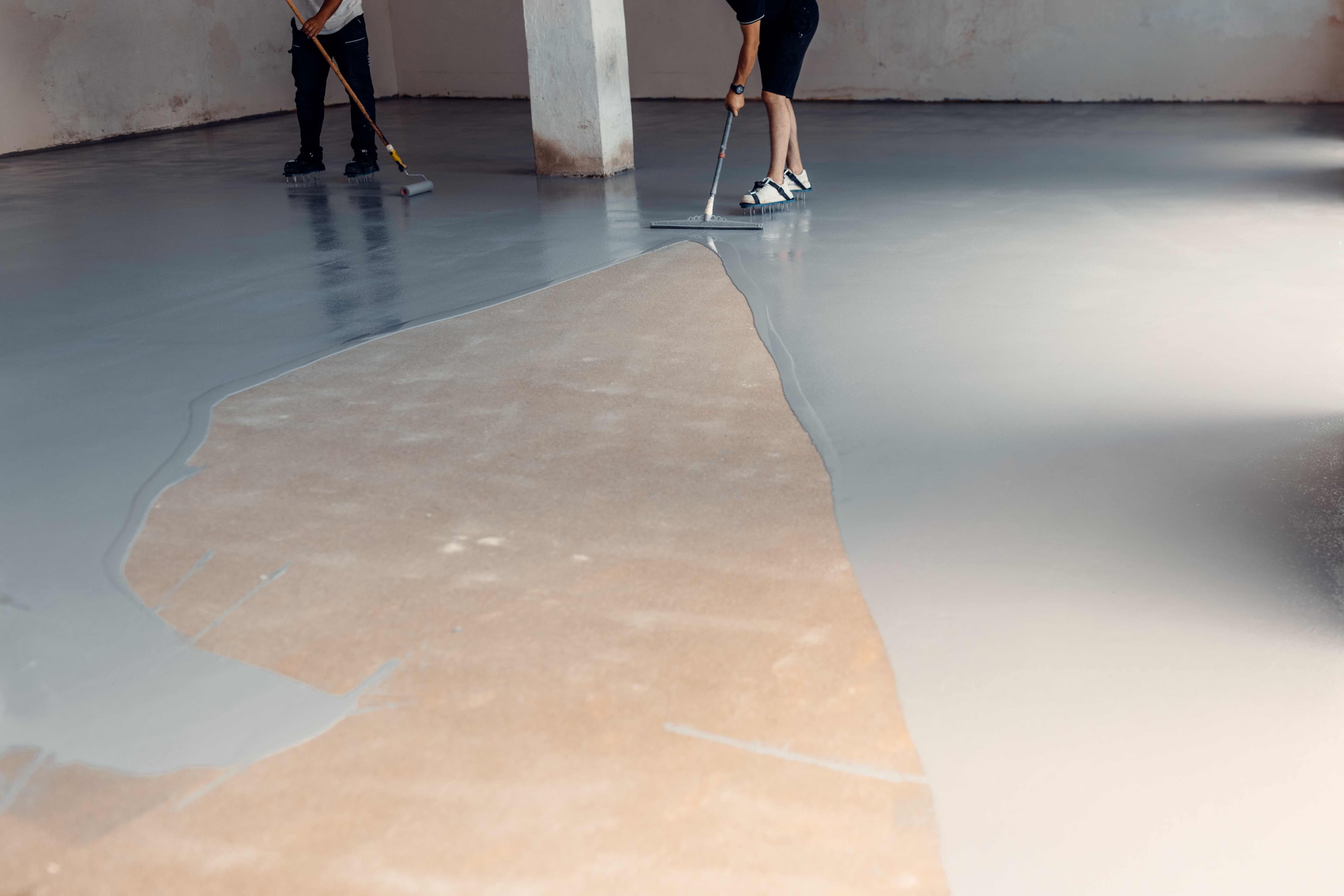 Workers rolling gray epoxy coating onto a concrete garage floor