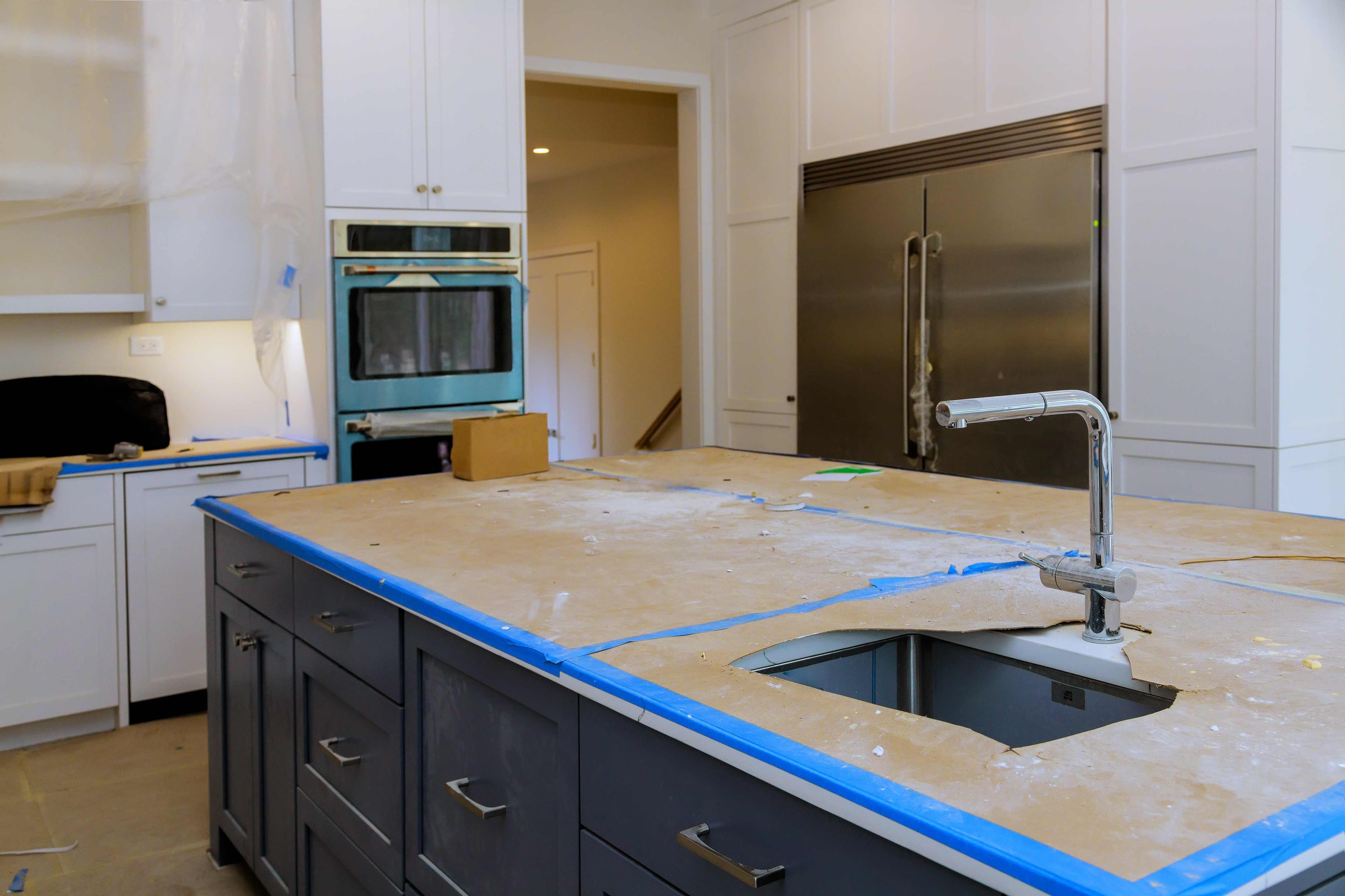 A kitchen island mid-renovation with the countertop edges taped off around a new sink and faucet cutout.