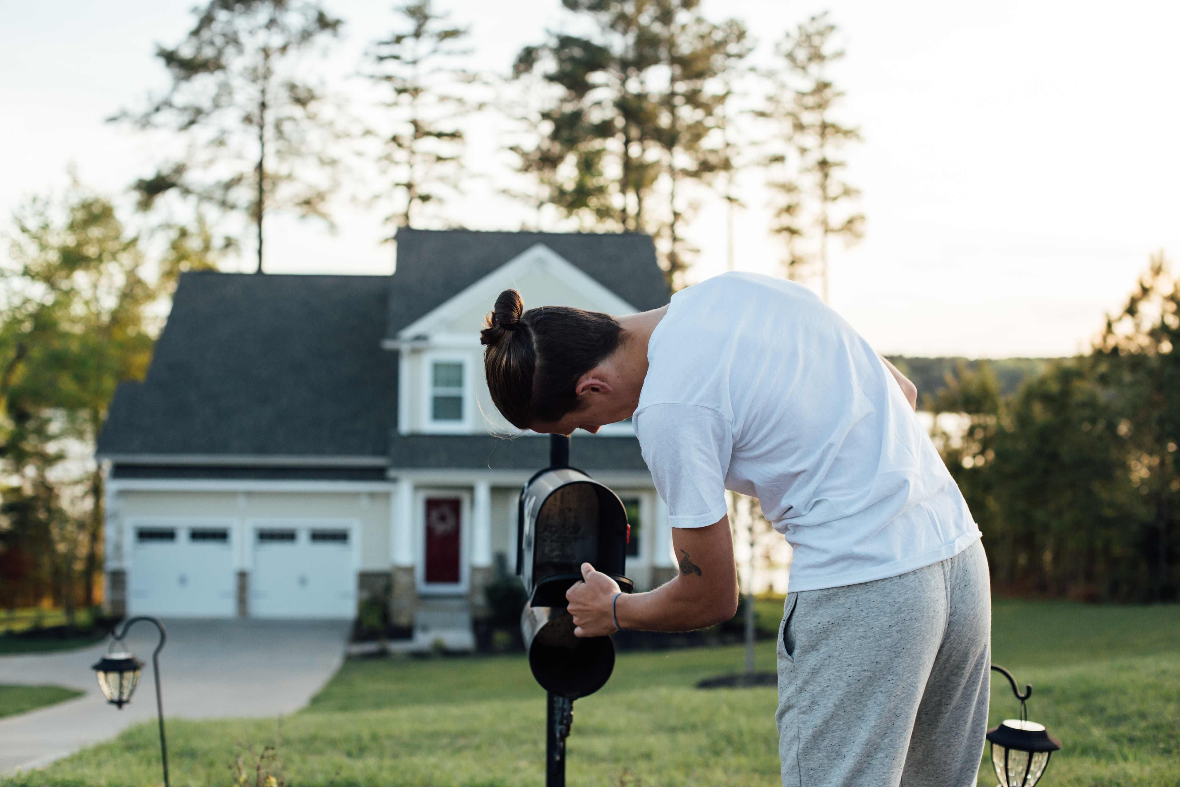 Person installing a mailbox post outdoors beside a residential driveway and yard