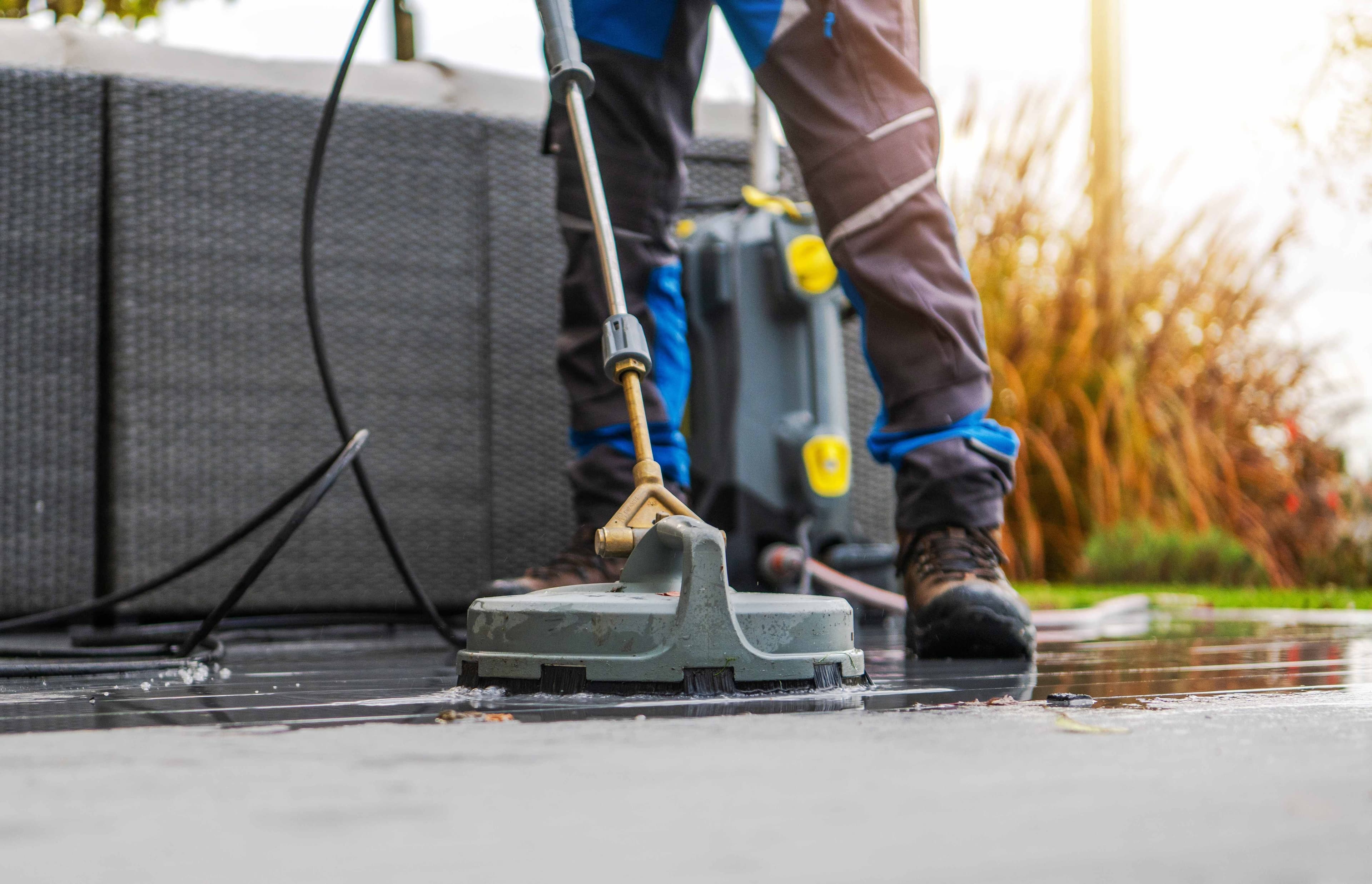 A close-up of a rotary surface cleaner attachment being used on an outdoor patio surface.