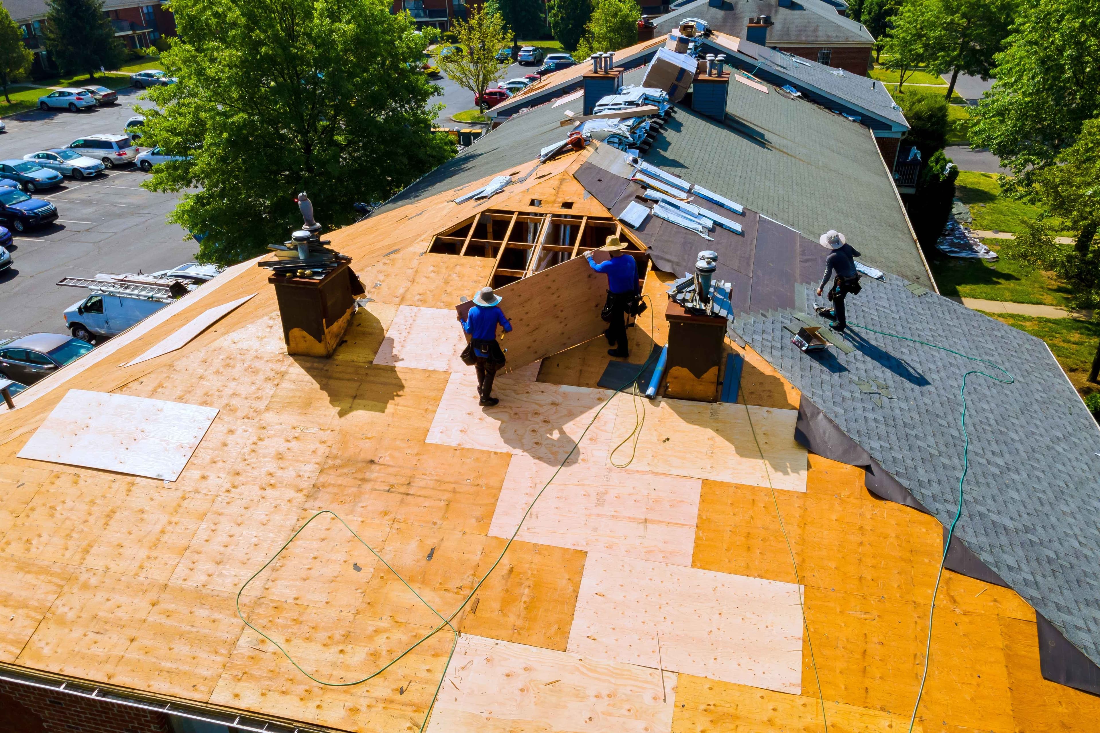 Aerial view of a residential roof during shingle installation, with plywood decking exposed and roofing material staged near the ridge.