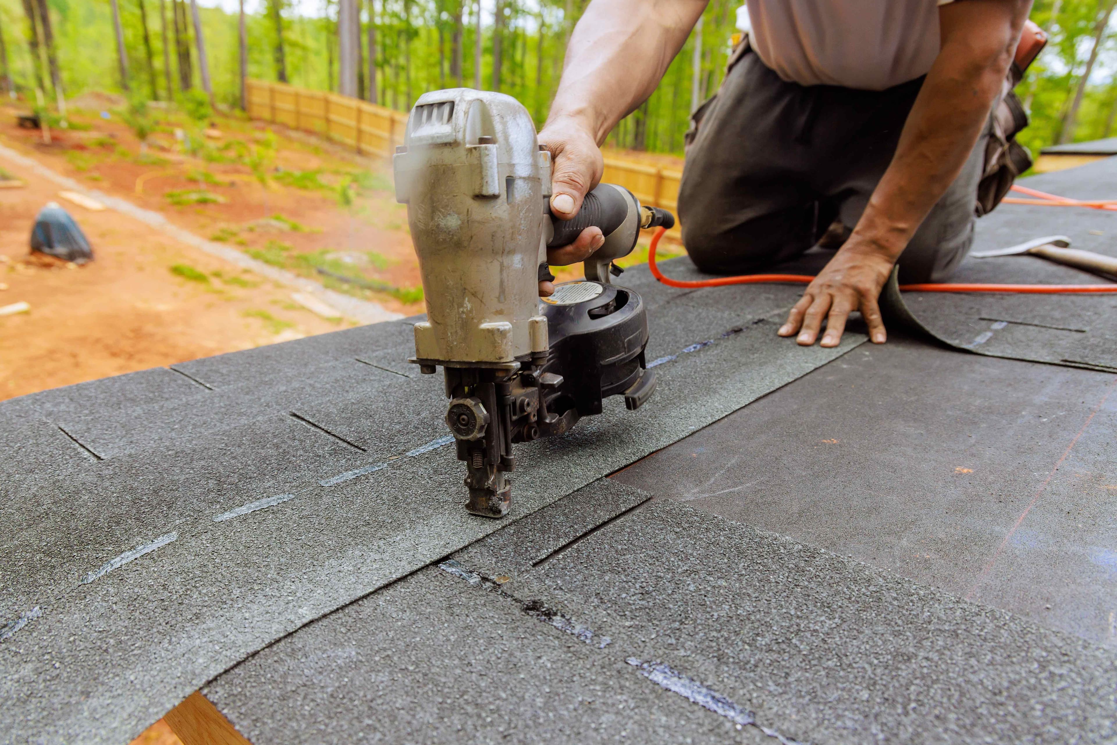 Close-up of a roofing nail gun securing an asphalt shingle during shingle repair work.