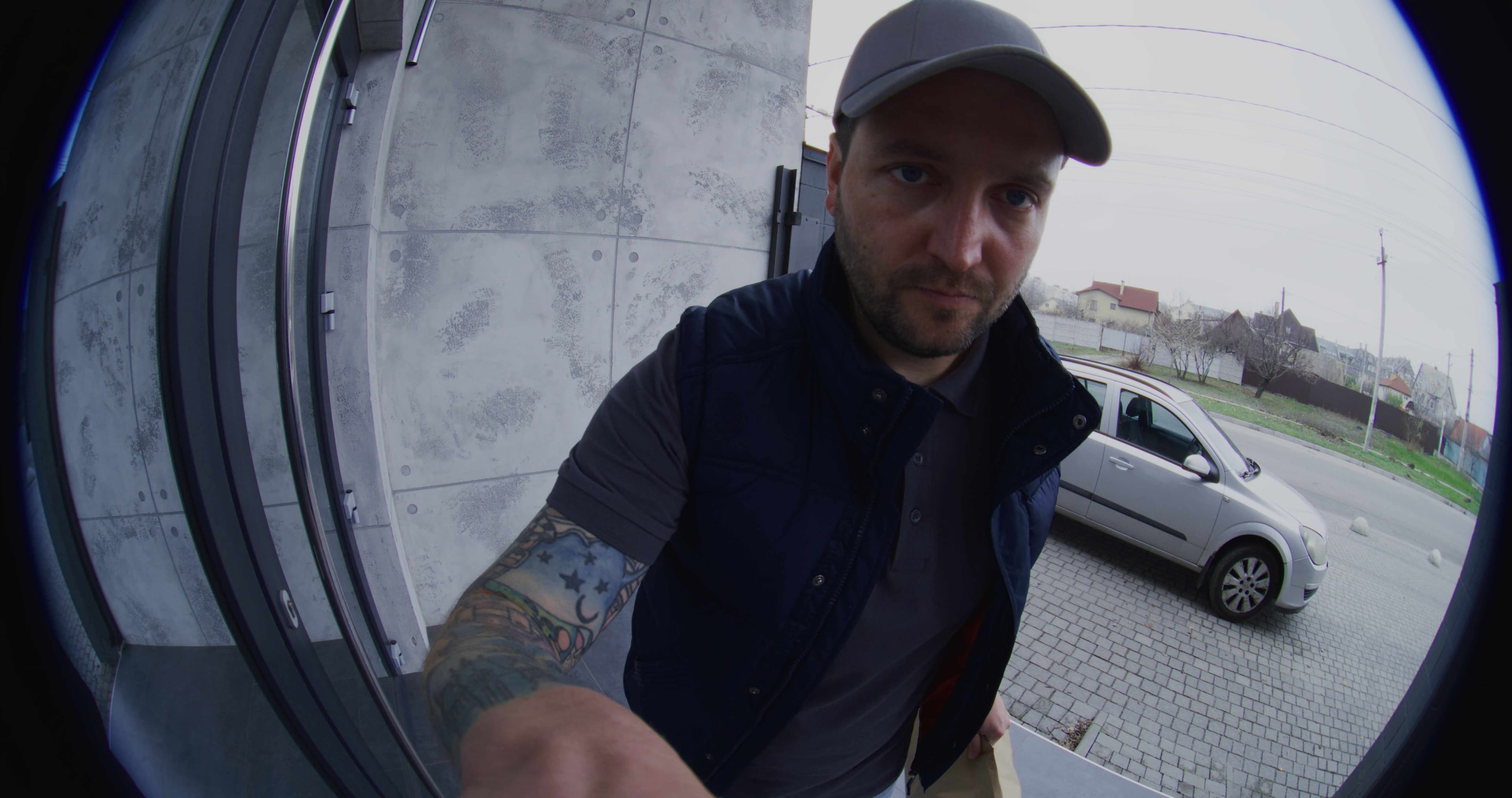 Wide-angle video doorbell camera view of a visitor reaching toward the doorbell at a front entrance.