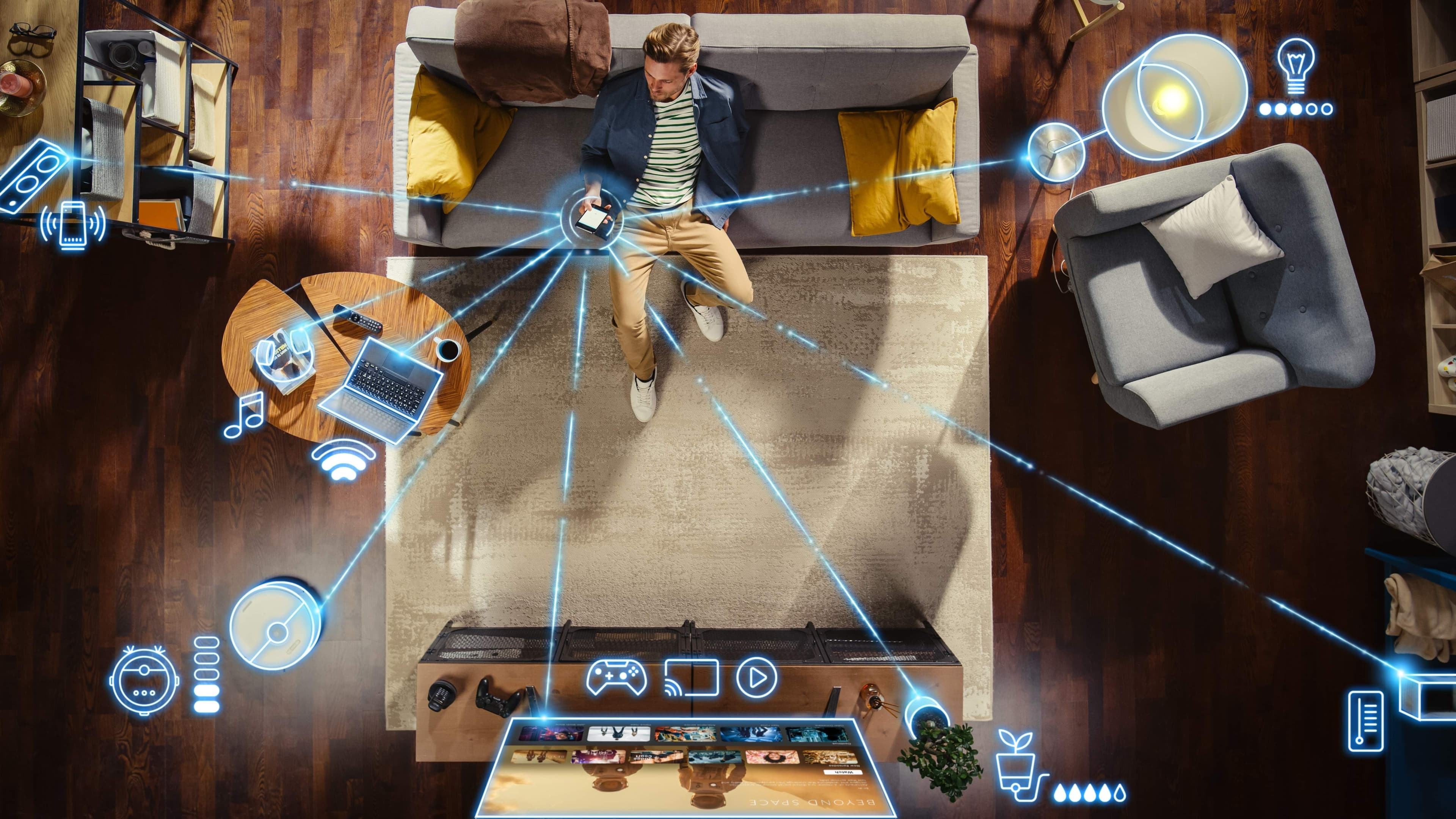 Overhead view of a living room where a person on a sofa holds a phone connected by glowing lines to smart speakers, lamps, a robot vacuum, a thermostat, and other connected devices.