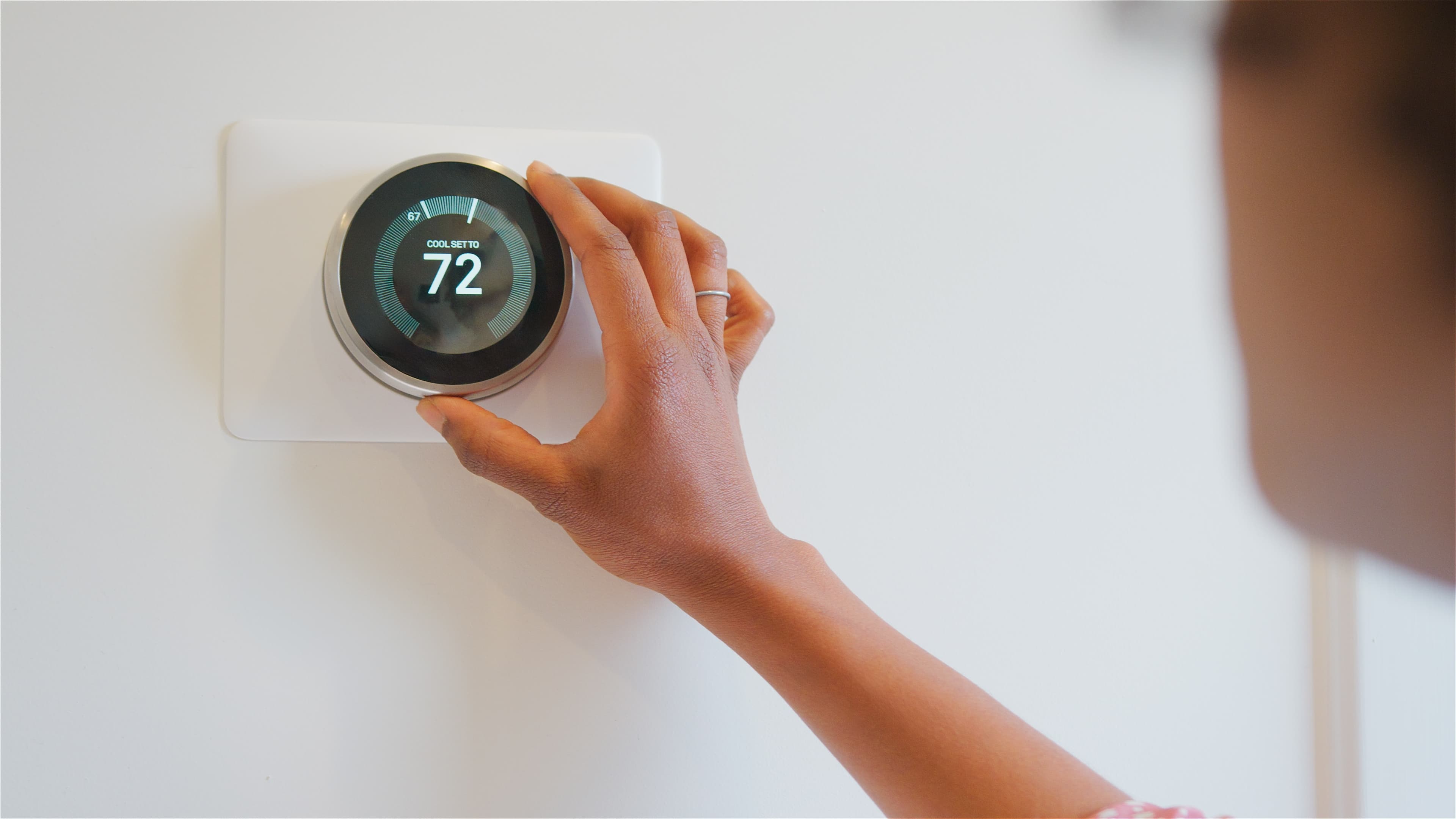 Hand adjusting a round smart thermostat on a wall