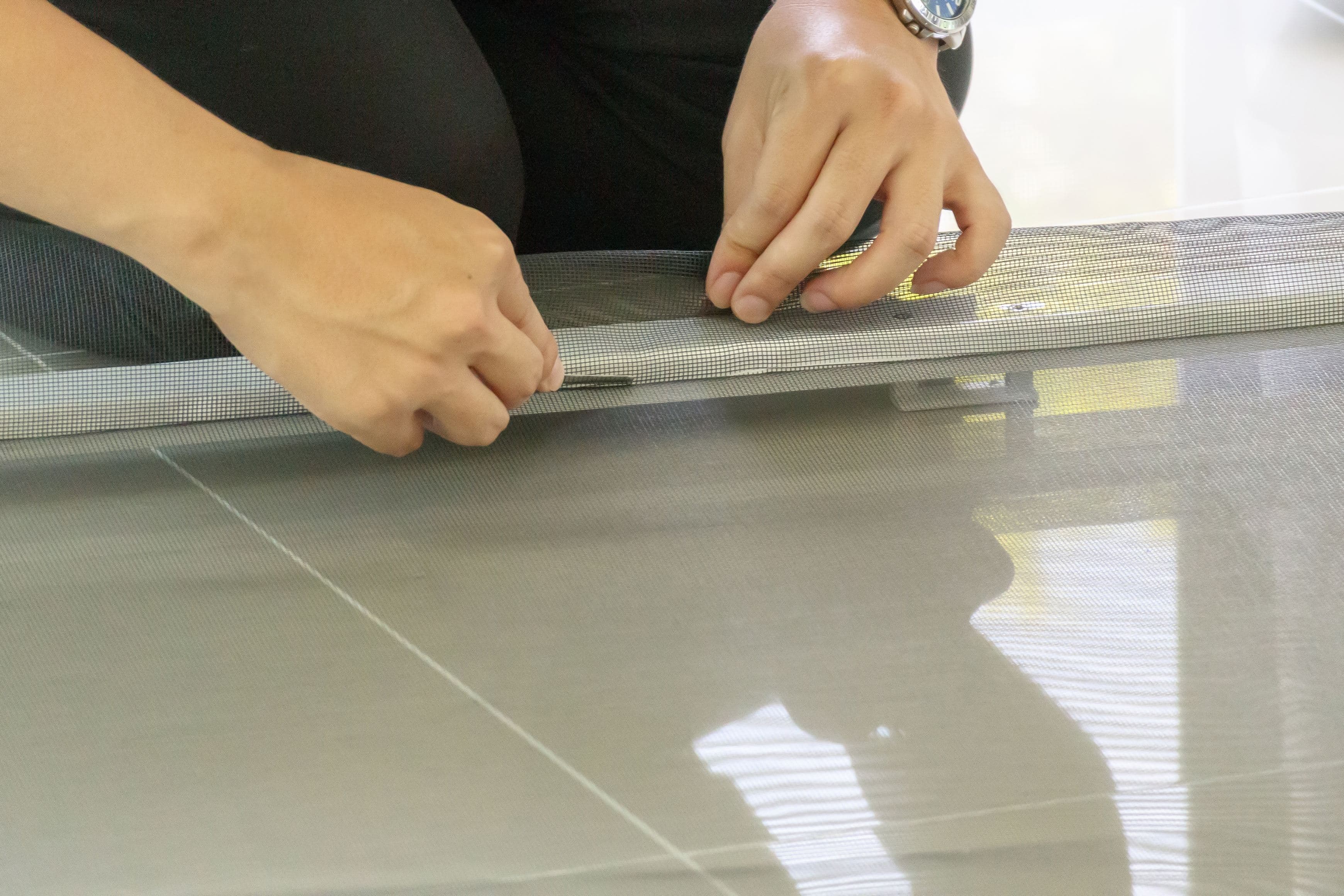 Hands pressing new screen mesh and spline into a window screen frame track