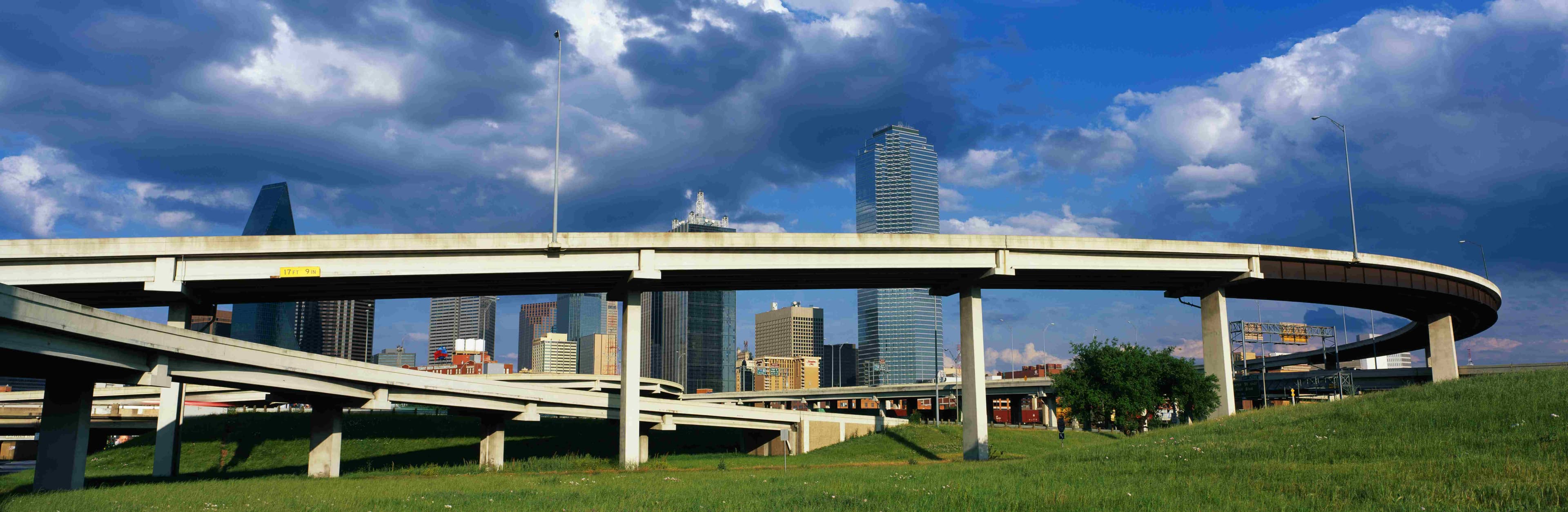 Dallas skyline and elevated highways beneath dramatic storm clouds