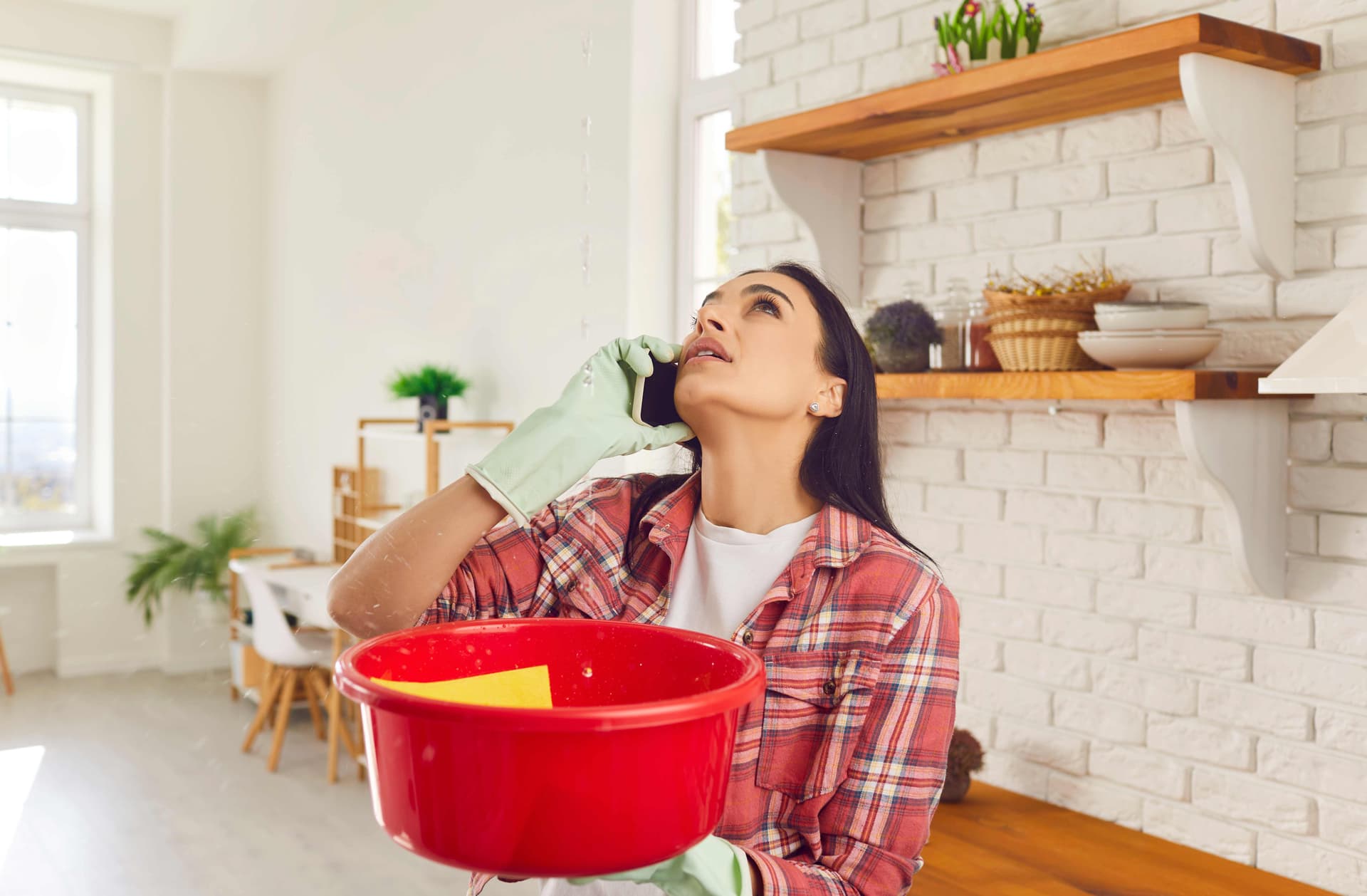 Woman with red bucket catching water from a ceiling leak while looking up