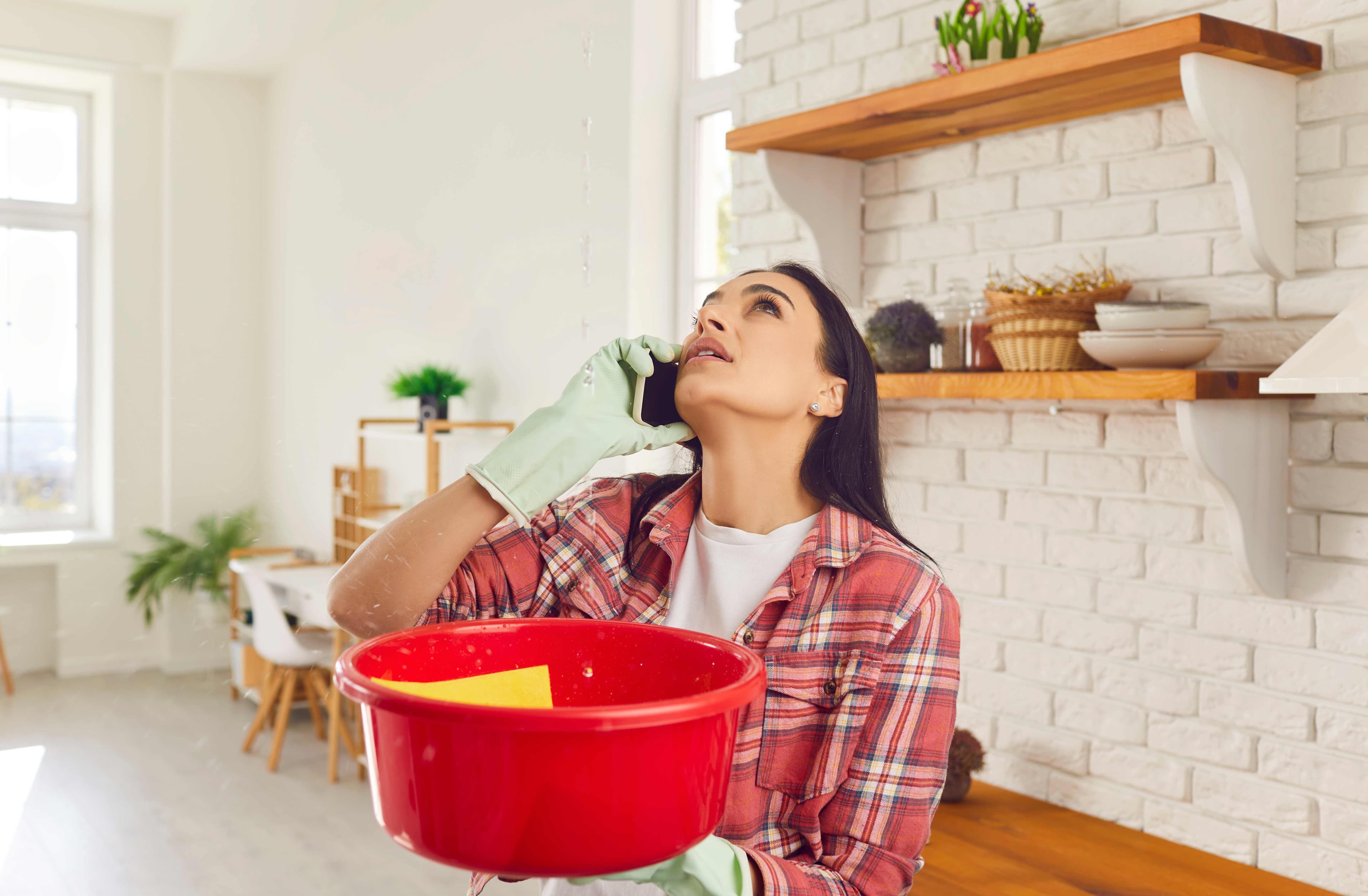Woman catching water from a ceiling leak while looking up