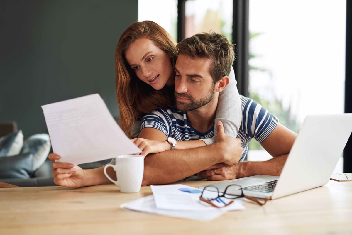 Couple reviewing home maintenance checklist and notes together at desk with laptop