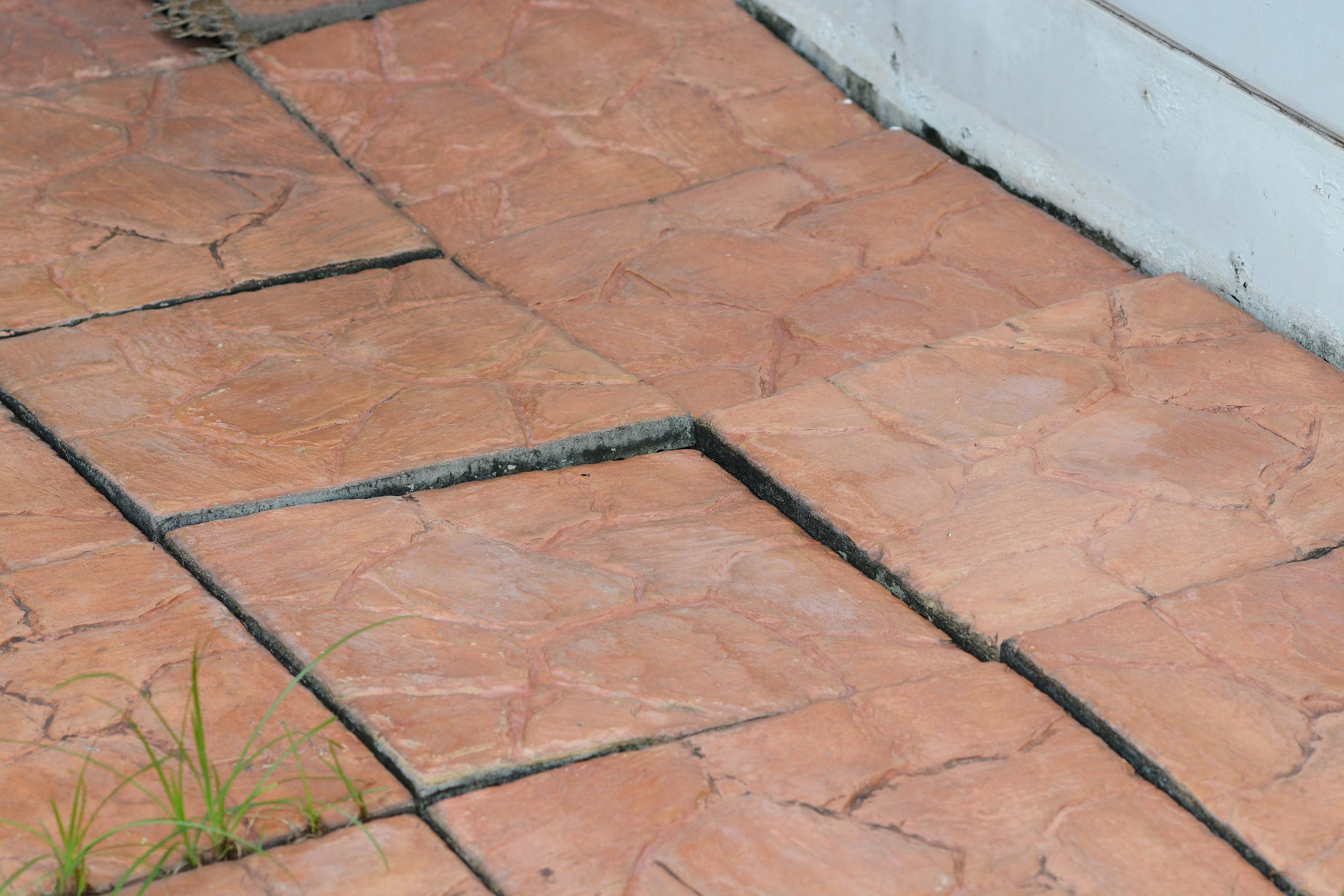 A visible crack running along a joint of a stamped concrete patio near the base of an exterior wall