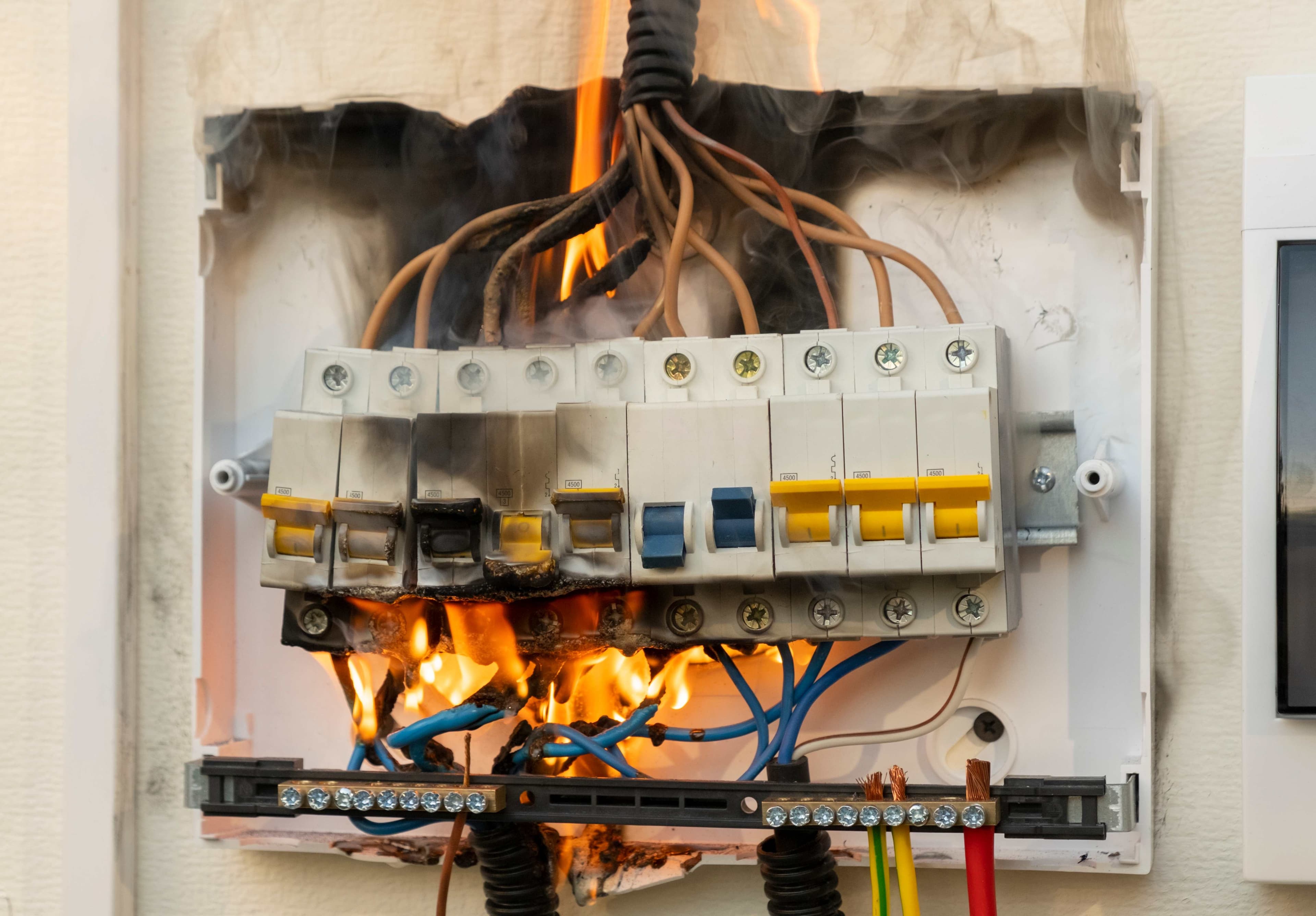 An electrical breaker panel with exposed wiring and visible flames and smoke