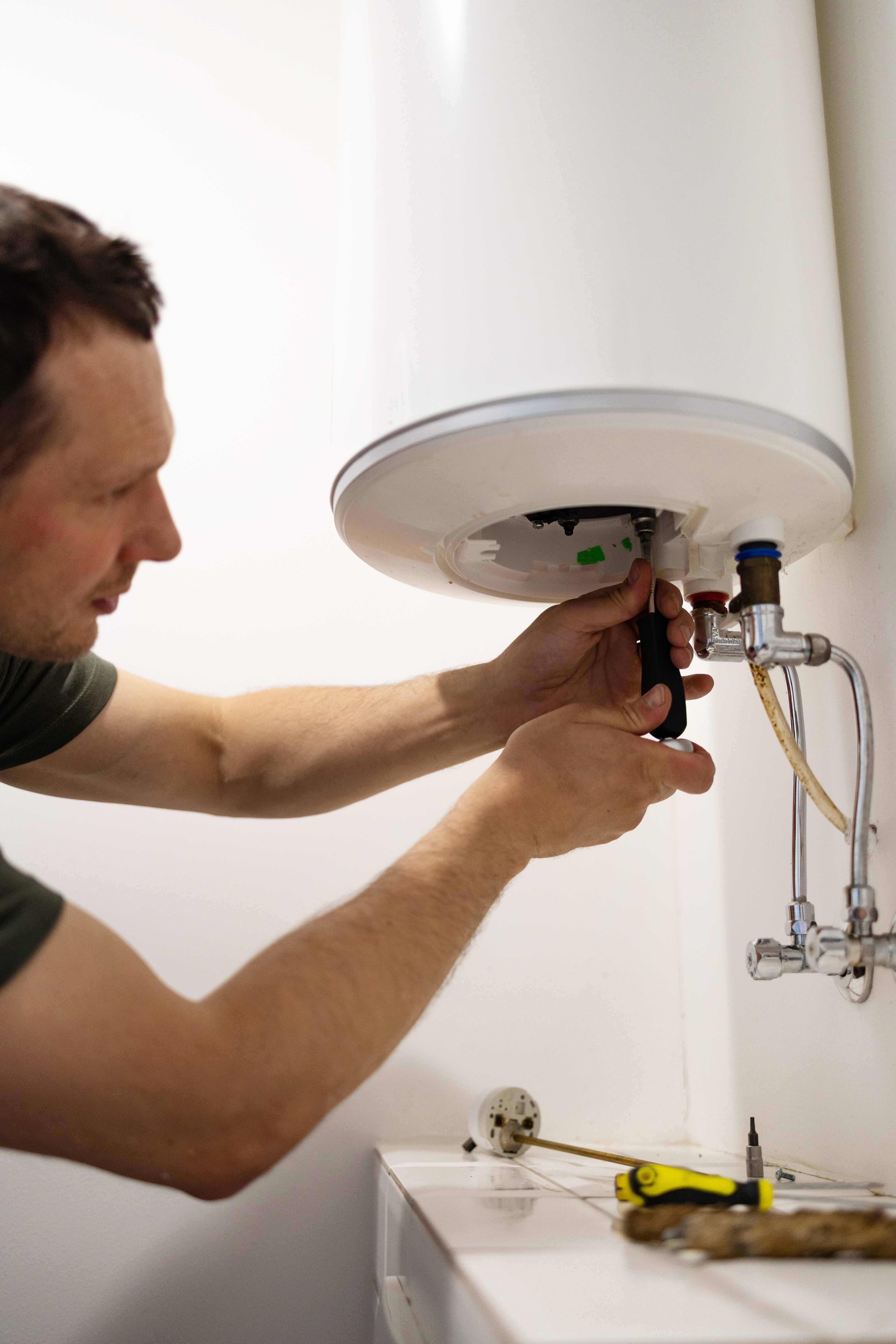 Technician servicing a residential water heater with hand tools